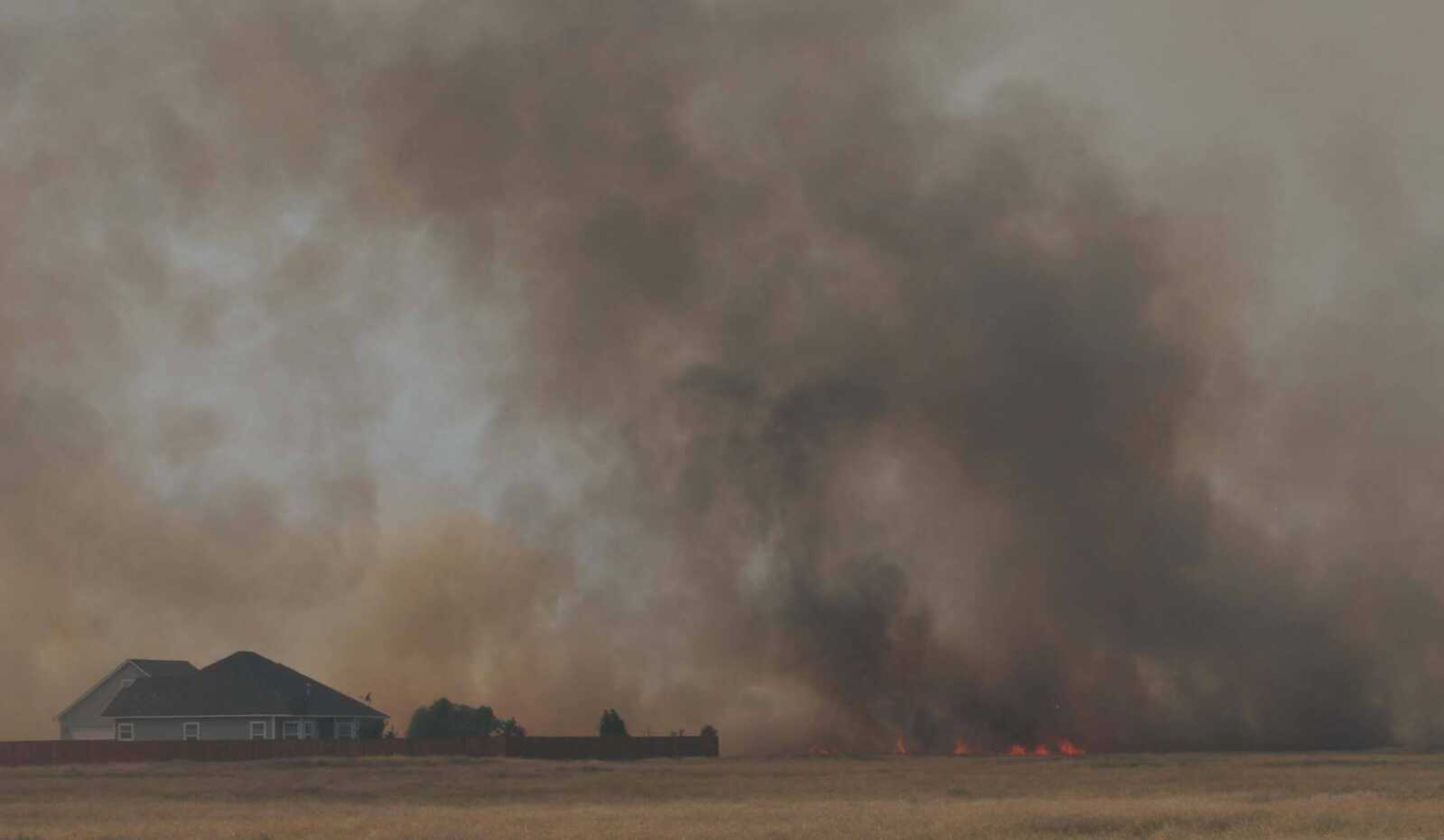 Smoke and flames threaten a home on Southwest Heaton Lane as the range fire swept through range land south of Mountain Home last week. <i><small>Photo by Brian S. Orban</i></small>