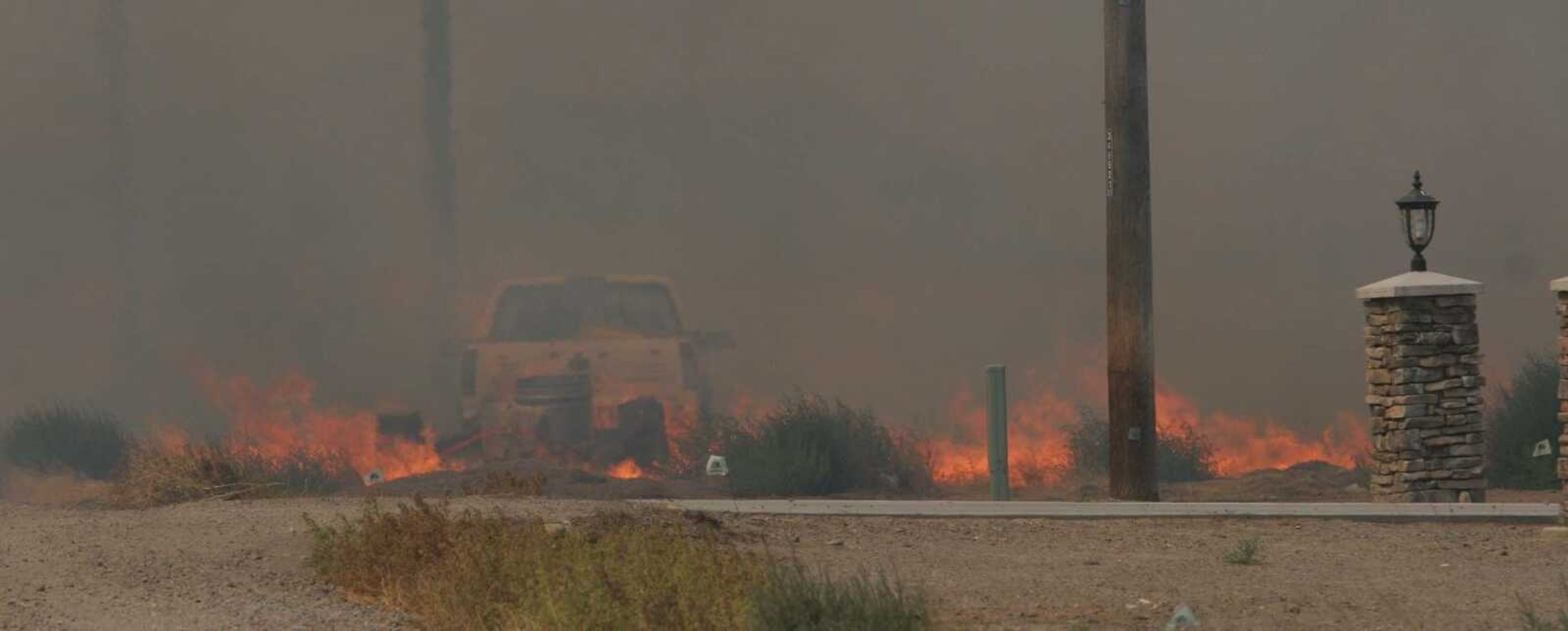 Flames engulf a vehicle as the range fire swept across Southwest Heaton Lane last week. Photo by Brian S. Orban