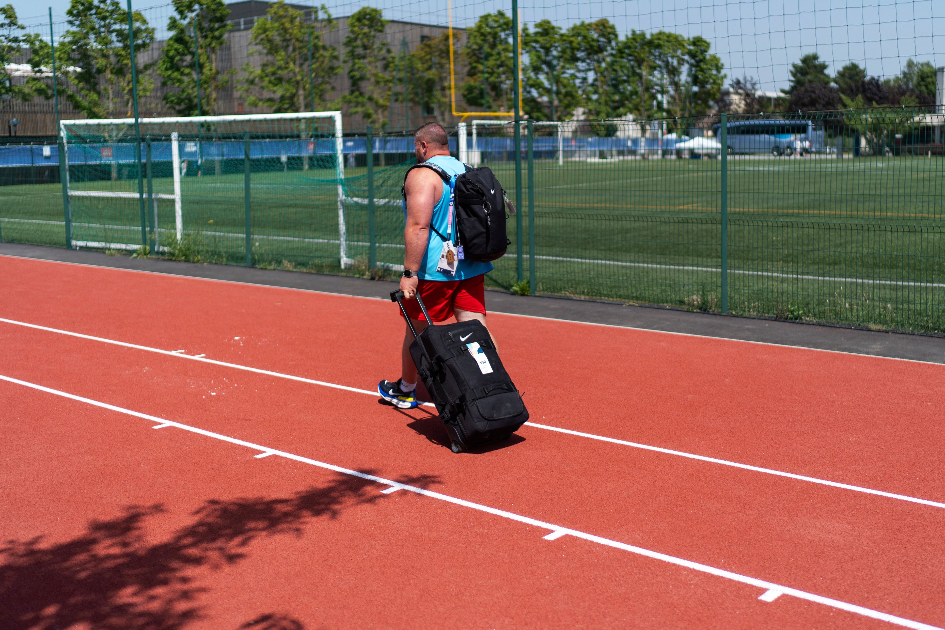 Shot putter Joe Kovacs walks off the field with his bags after a practice session at the Team USA training facility at the 2024 Summer Olympics, Tuesday, July 30, 2024, in Eaubonne, France. (AP Photo/David Goldman)