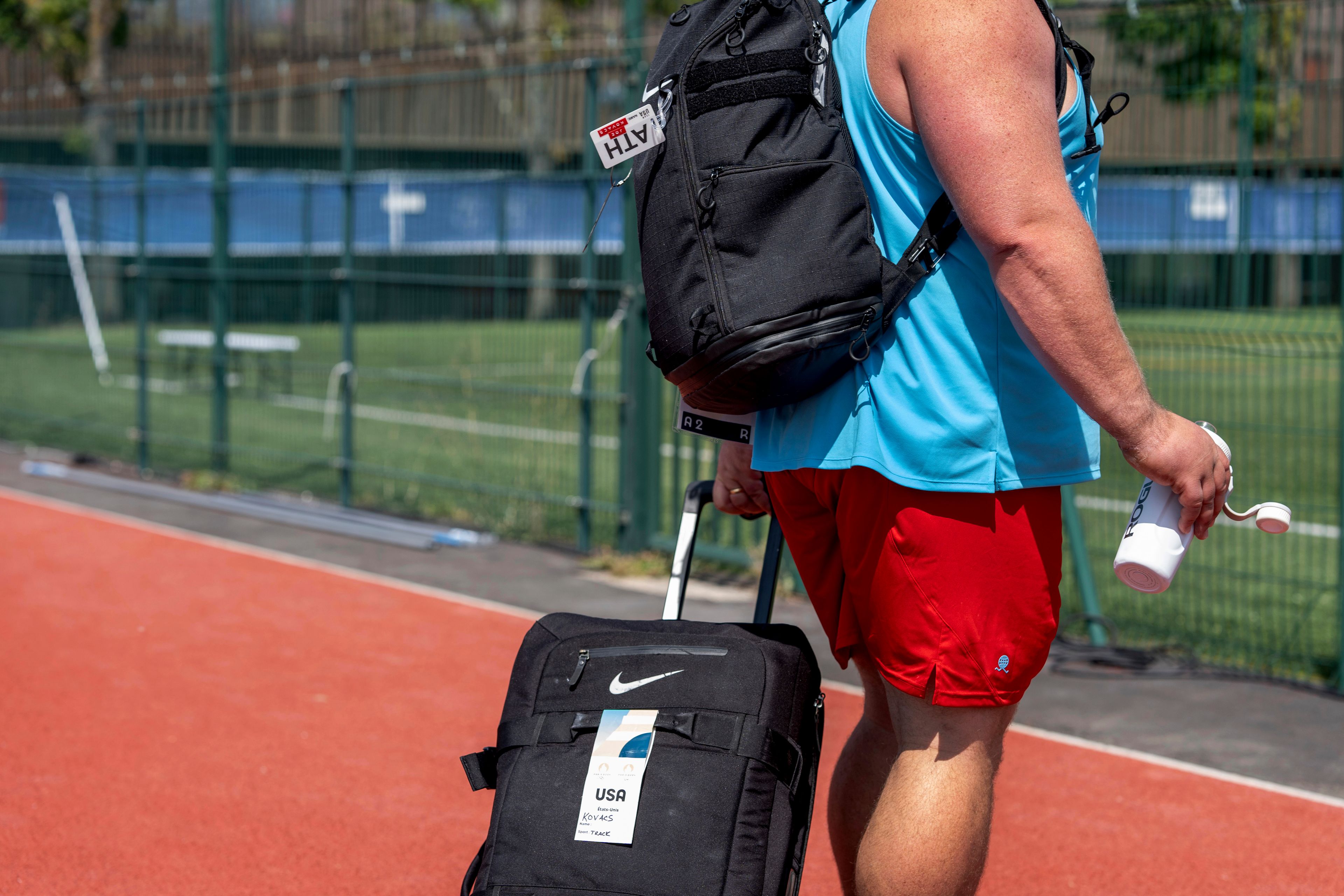 Luggage tags are seen on the bags of shot putter Joe Kovacs as he walks off the field after a practice session at the Team USA training facility at the 2024 Summer Olympics, Tuesday, July 30, 2024, in Eaubonne, France. (AP Photo/David Goldman)