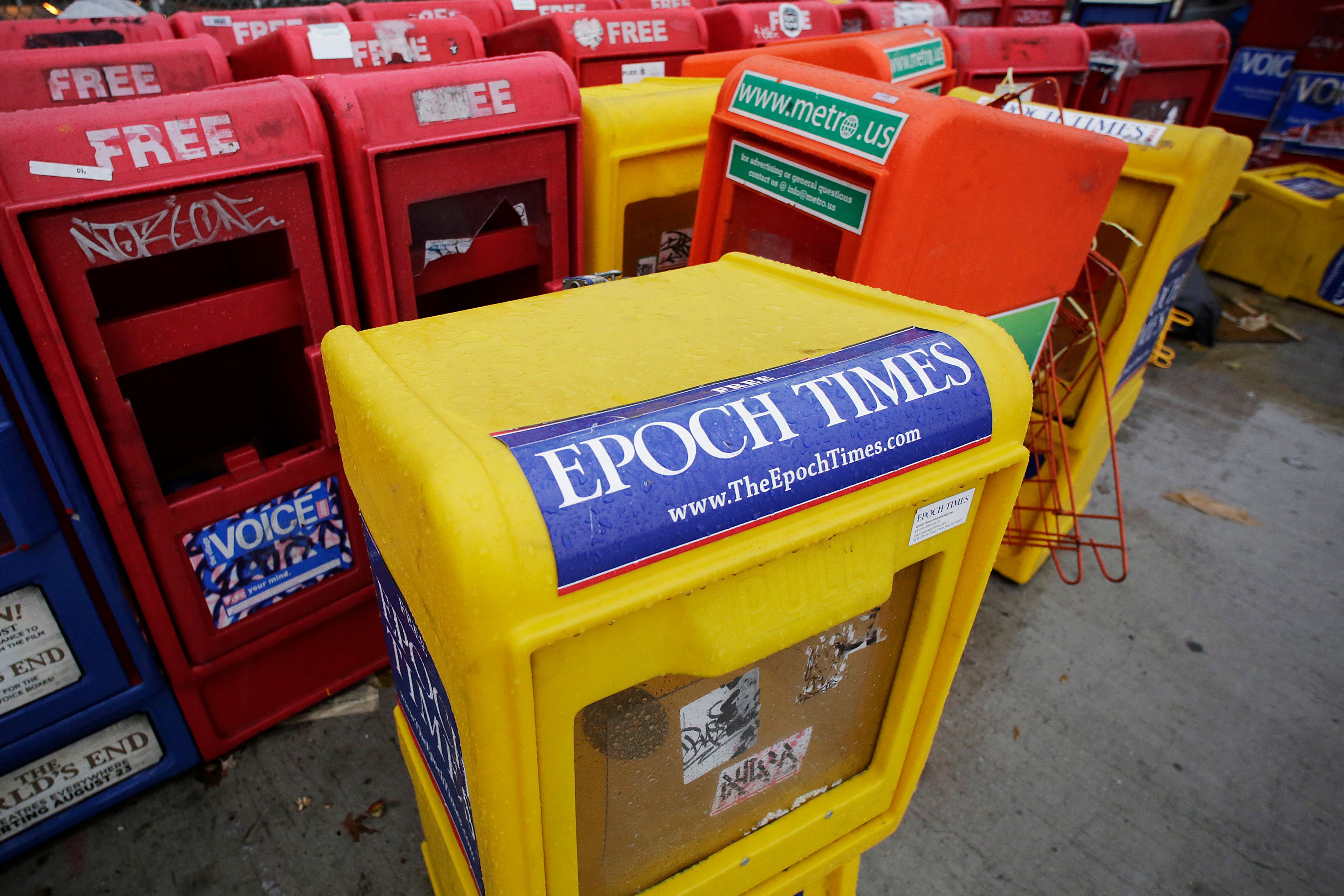 FILE - Plastic newspaper racks for The Epoch Times, The Village Voice and other newspapers stand along a Manhattan sidewalk, Wednesday, Nov. 27, 2013 in New York. The arrest of an executive at The Epoch Times in a money-laundering scheme this week has drawn attention to a media outlet that has largely lived in the shadows between its founding in 2000 and a transformation during the Trump administration.