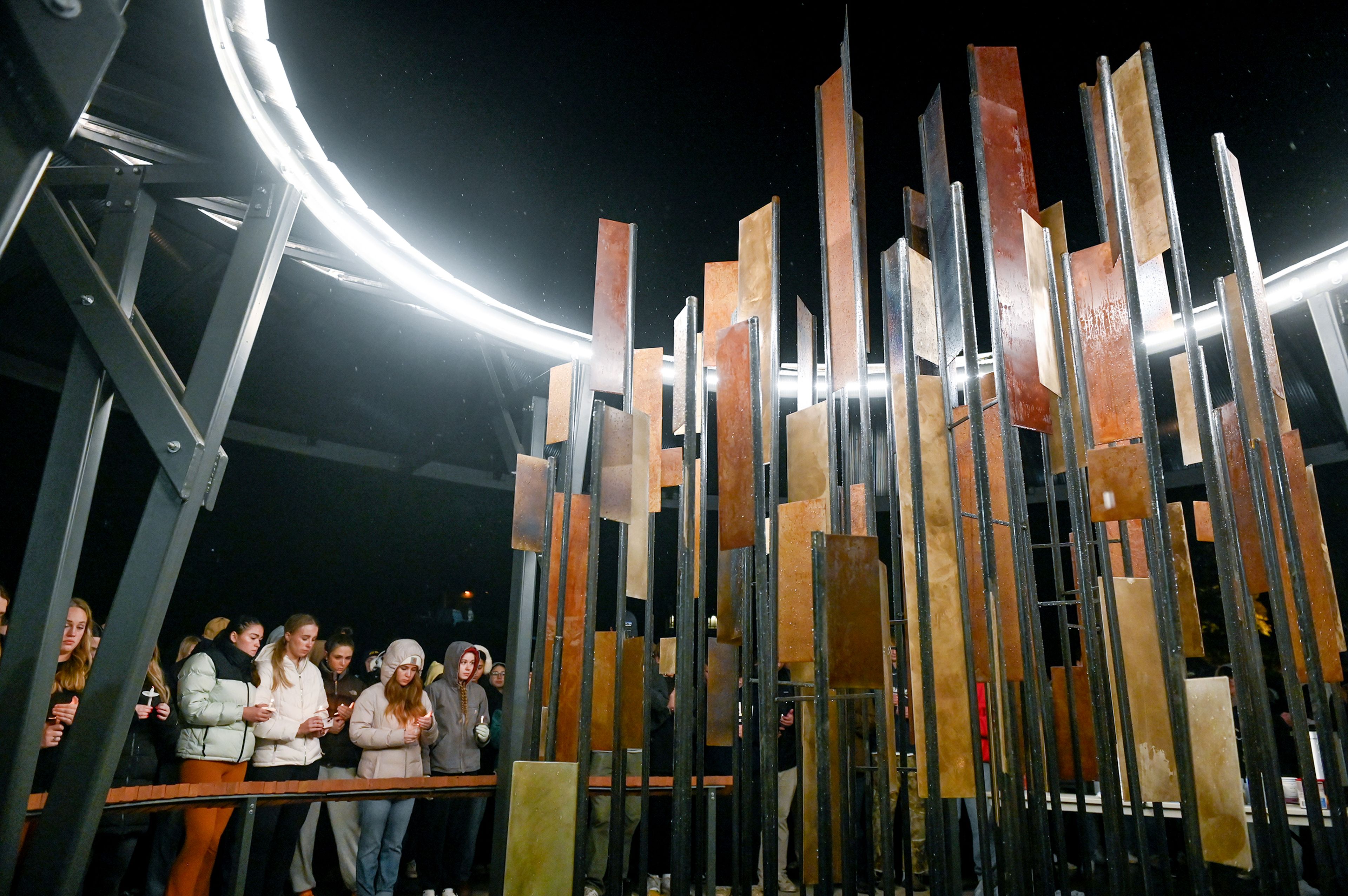 Those gathered for a vigil marking two years since the murder of four University of Idaho students stand in front of their names and the sculpture dedicated to the four lost at the Vandal Healing Garden and Memorial Wednesday in Moscow.