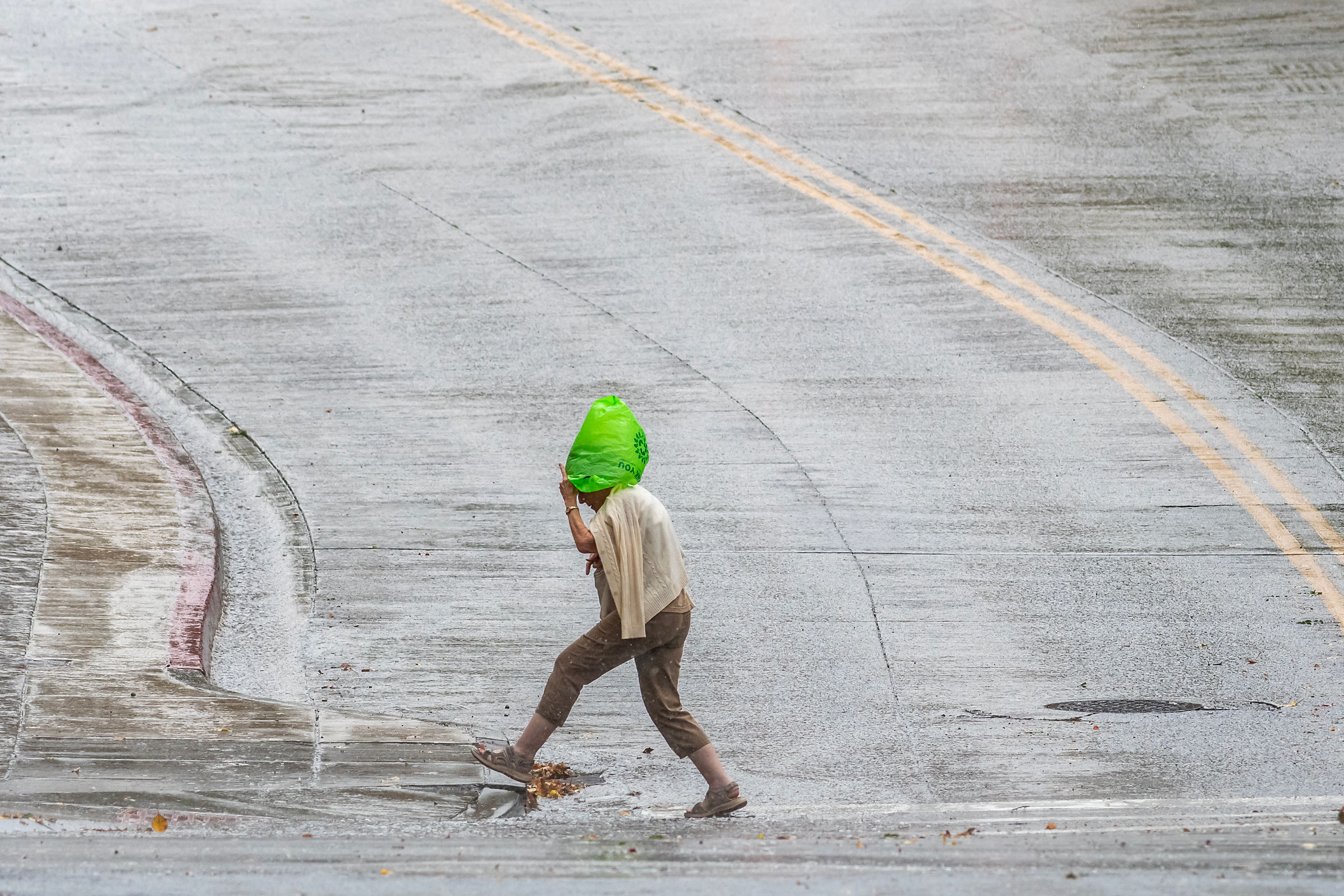 A person steps up onto a curb while crossing the intersection of Fifth and Main streets using a bag to shield themselves from the rain Wednesday in Lewiston.