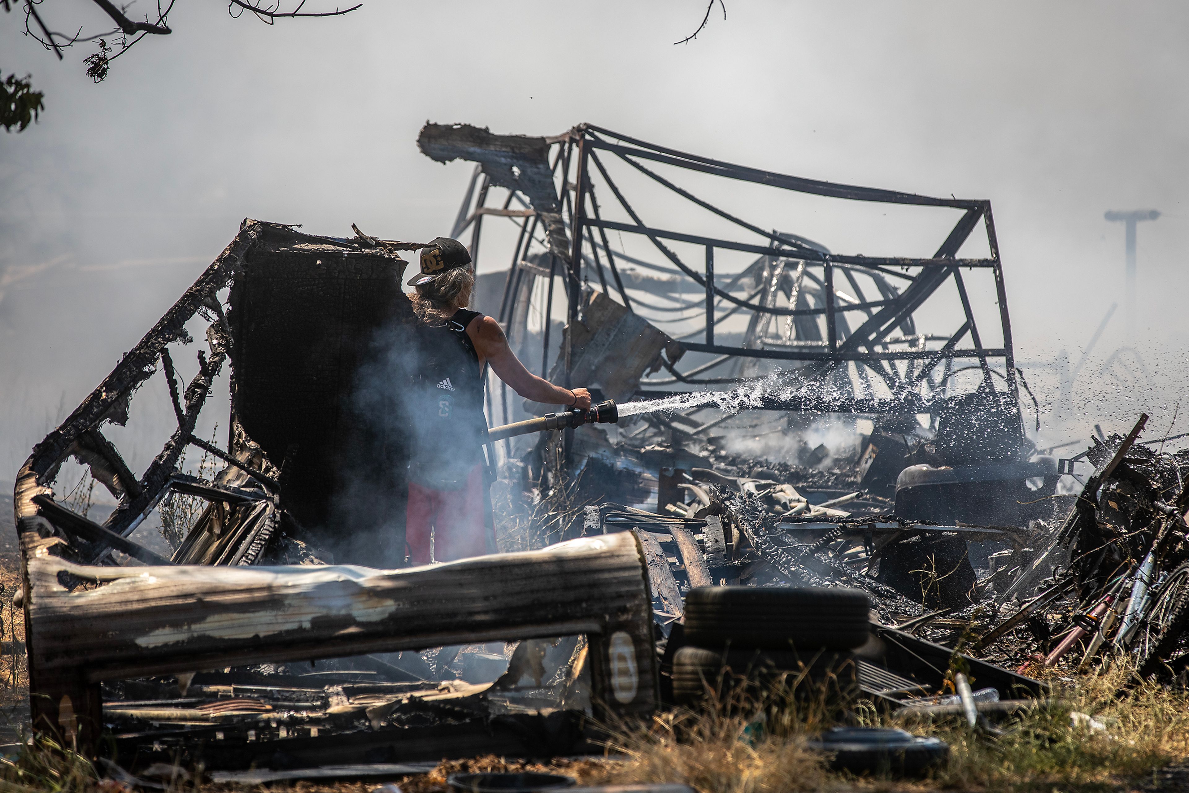 A person sprays down burned remains of a home at the scene of a structure fire Friday on Lolo Street in Lapwai.