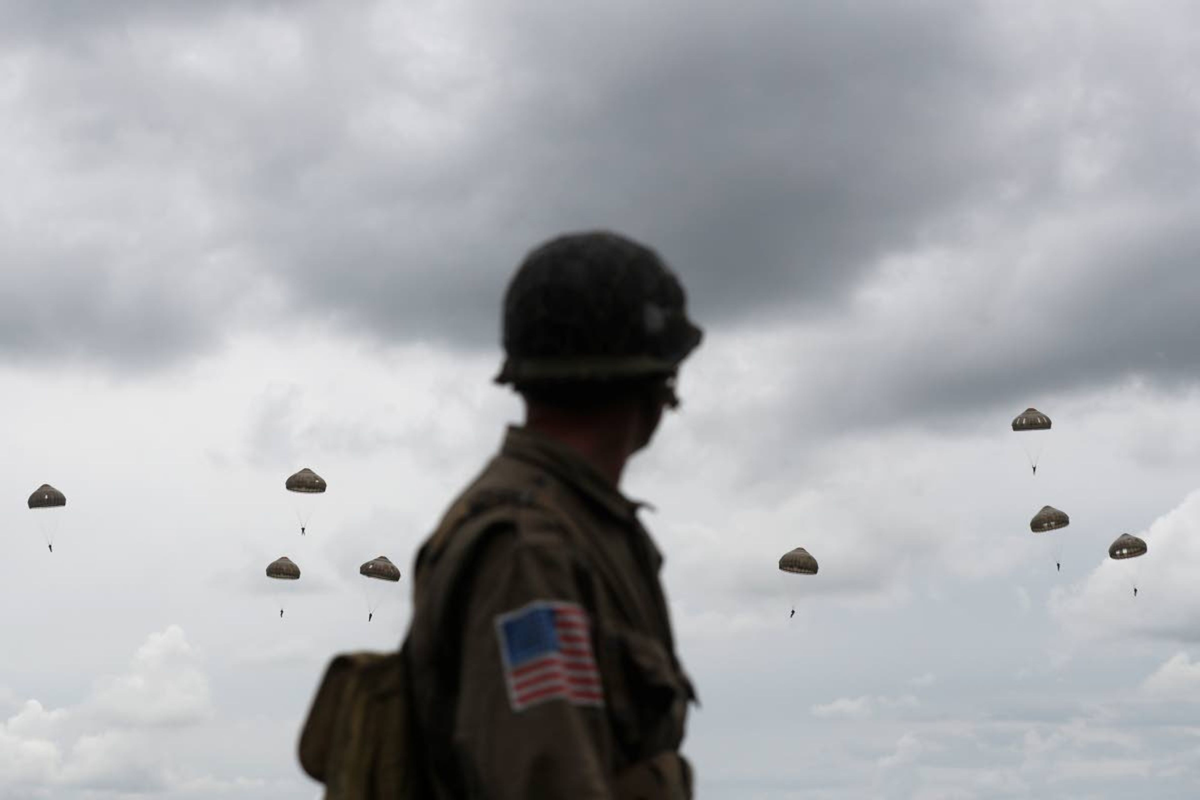 A WWII enthusiasts watches French and British parachutists jumping during a commemorative parachute jump over Sannerville, Normandy, Wednesday, June 5, 2019. Extensive commemorations are being held in the U.K. and France to honor the nearly 160,000 troops from Britain, the United States, Canada and other nations who landed in Normandy on June 6, 1944 in history's biggest amphibious invasion. (AP Photo/Thibault Camus)