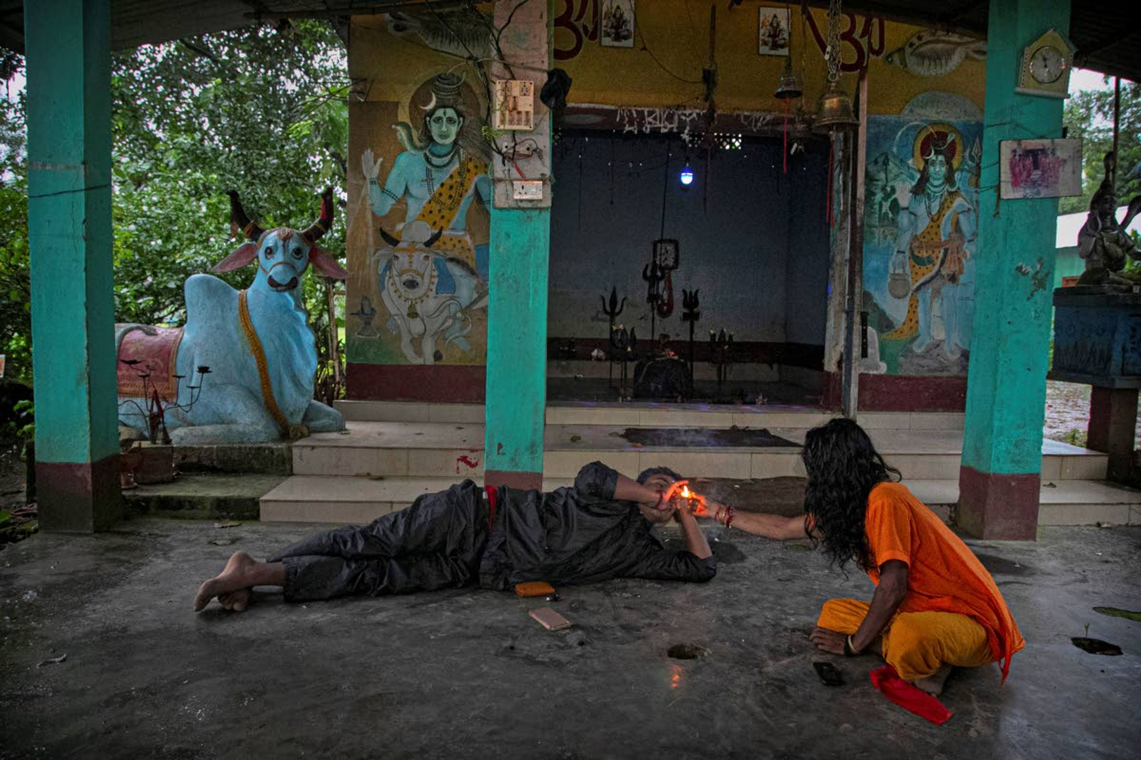 Ramananda Sarkar, 43, smokes marijuana as he takes shelter at a temple of Hindu god Shiva during rainfall after making a trip to his village to meet his family early morning in Diprang village, in the northeastern Indian state of Assam, Tuesday, Sept. 22, 2020. While Hindu's believe cremation rights are sacred and release the dead person's soul from the cycle of rebirth, those who actually deal with corpses are looked down upon. After a month and a half of not seeing his wife and three sons, Sarkar snuck into his village in the middle of a recent rainy night. He called out to his family from the road outside his house and was able to spend 15 minutes with them and leave them some money. (AP Photo/Anupam Nath)