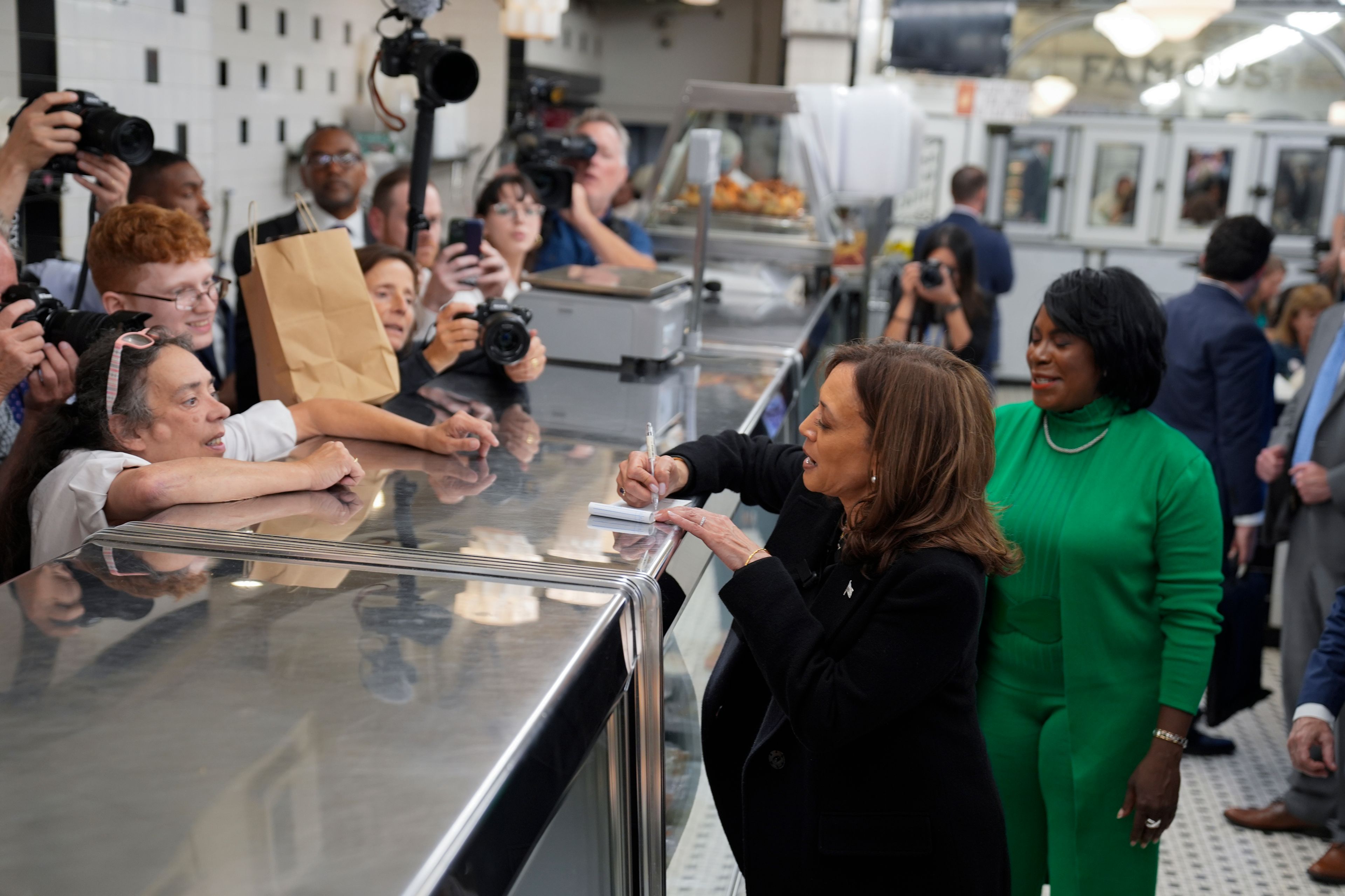 Democratic presidential nominee Vice President Kamala Harris, with Philadelphia Mayor Cherelle Parker, right, signs an autograph and speaks to workers and patrons at a campaign stop at Famous 4th Street Delicatessen in Philadelphia, Wednesday, Oct. 23, 2024. (AP Photo/Matt Rourke)