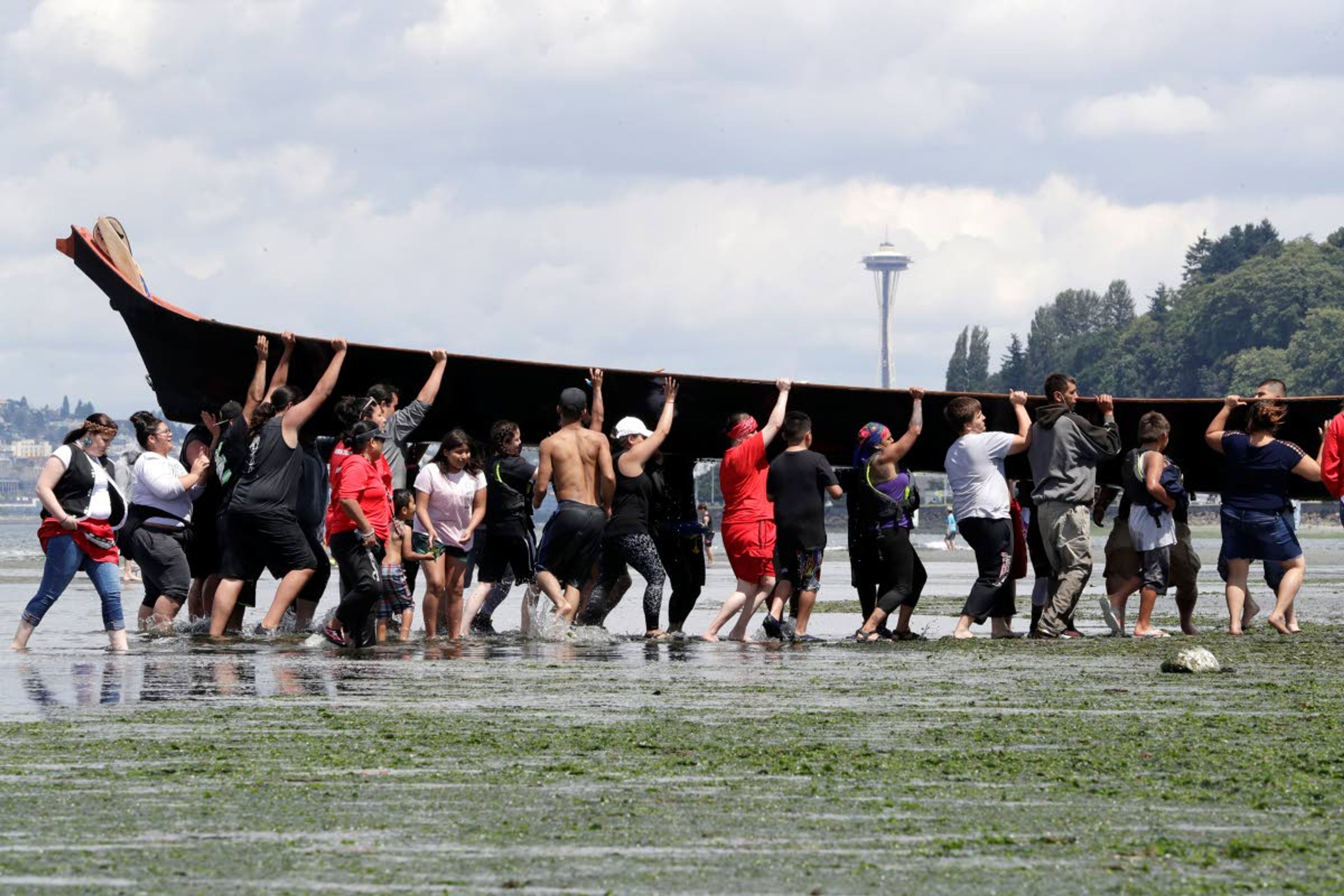 Canoe pullers and volunteers heft a canoe, with a view of the Space Needle in the background, during a stop on the annual tribal canoe journey through the Salish Sea on Thursday in Seattle.