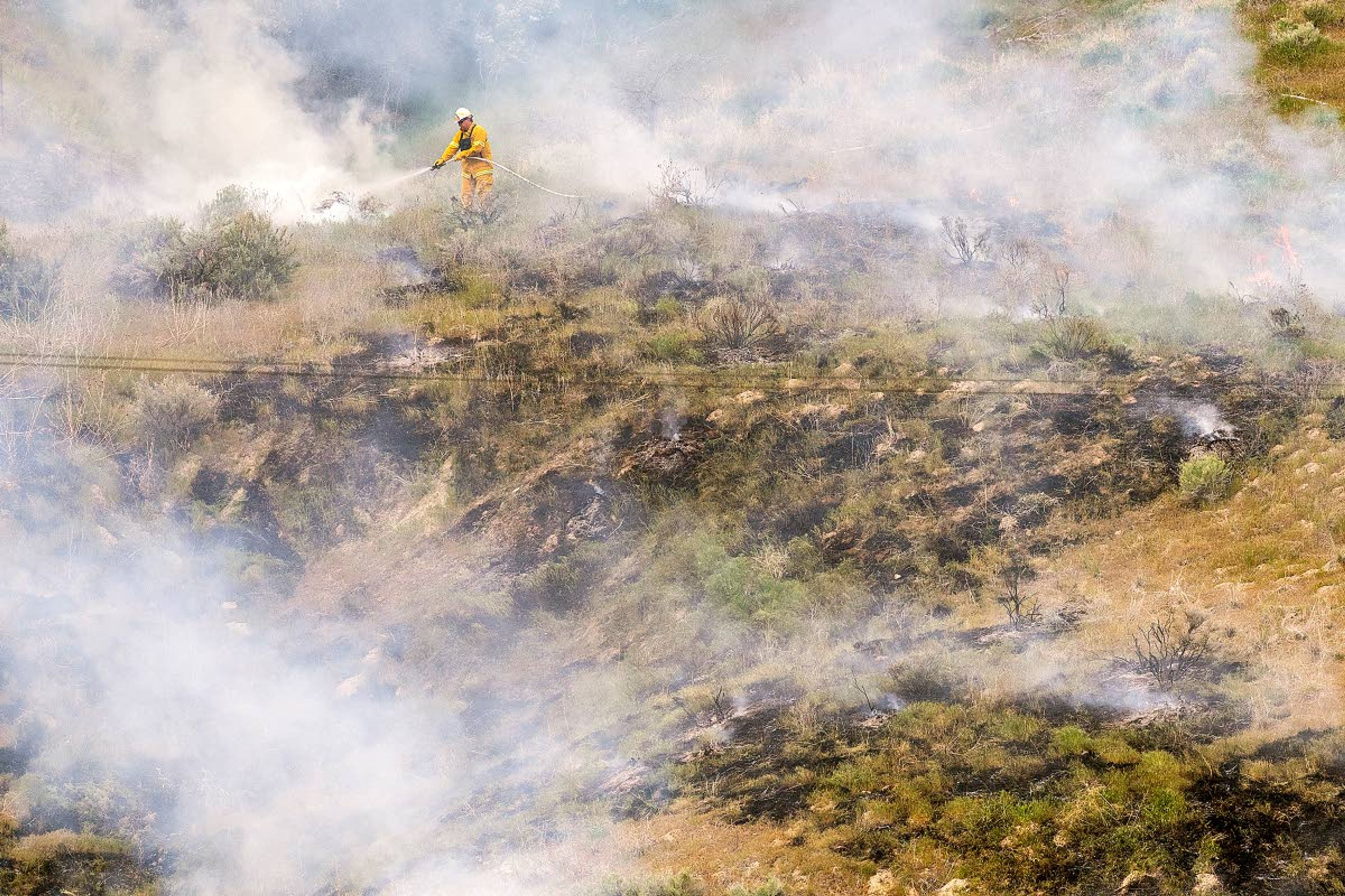 Surrounded by smoke, a firefighter from Asotin County Fire District No. 1 puts out hot spots along a ridge overlooking the Snake River northwest of Chief Timothy Park Wednesday afternoon west of Clarkston. Officials believe the fire started after a power line broke on the south side of the river across U.S. Highway 12 and sparked the small blaze that had burned about three-quarters of an acre of land.