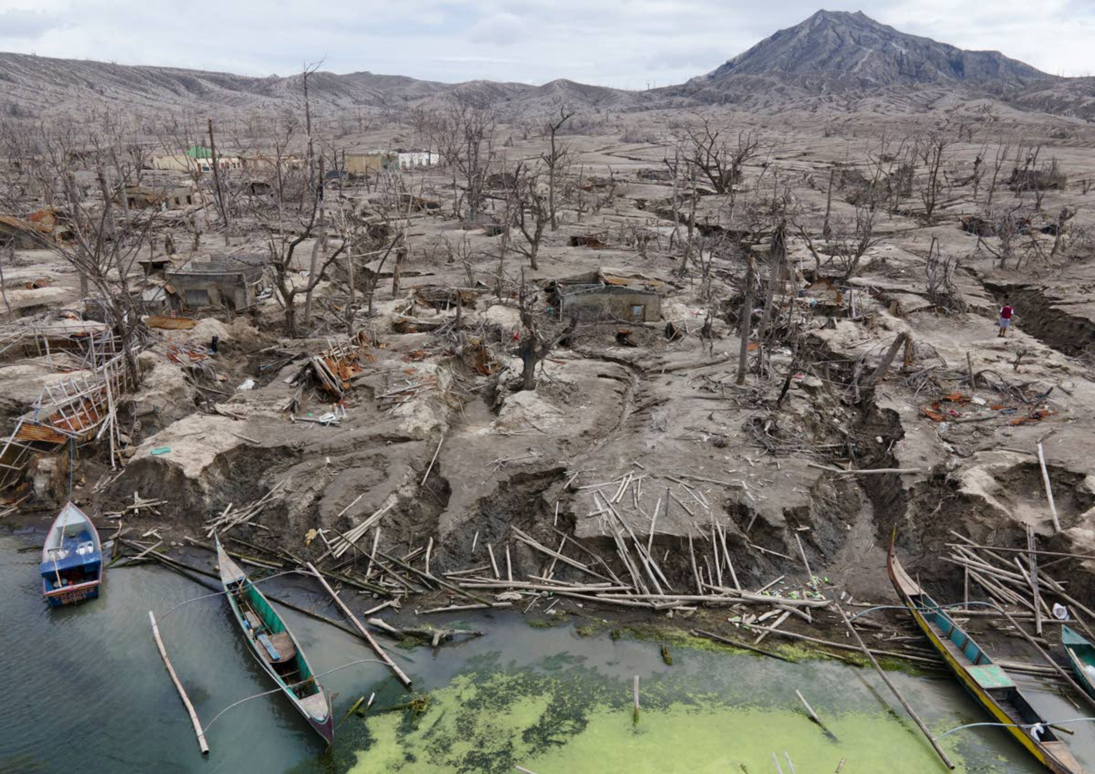 ABOVE: John Paulo Silva, a former resident at Taal volcano, brushes his teeth Jan. 10 outside his family’s tent at a relocation site in Balete, Batangas province, Philippines.LEFT: Houses damaged by ash and mud are seen at the Taal volcano.