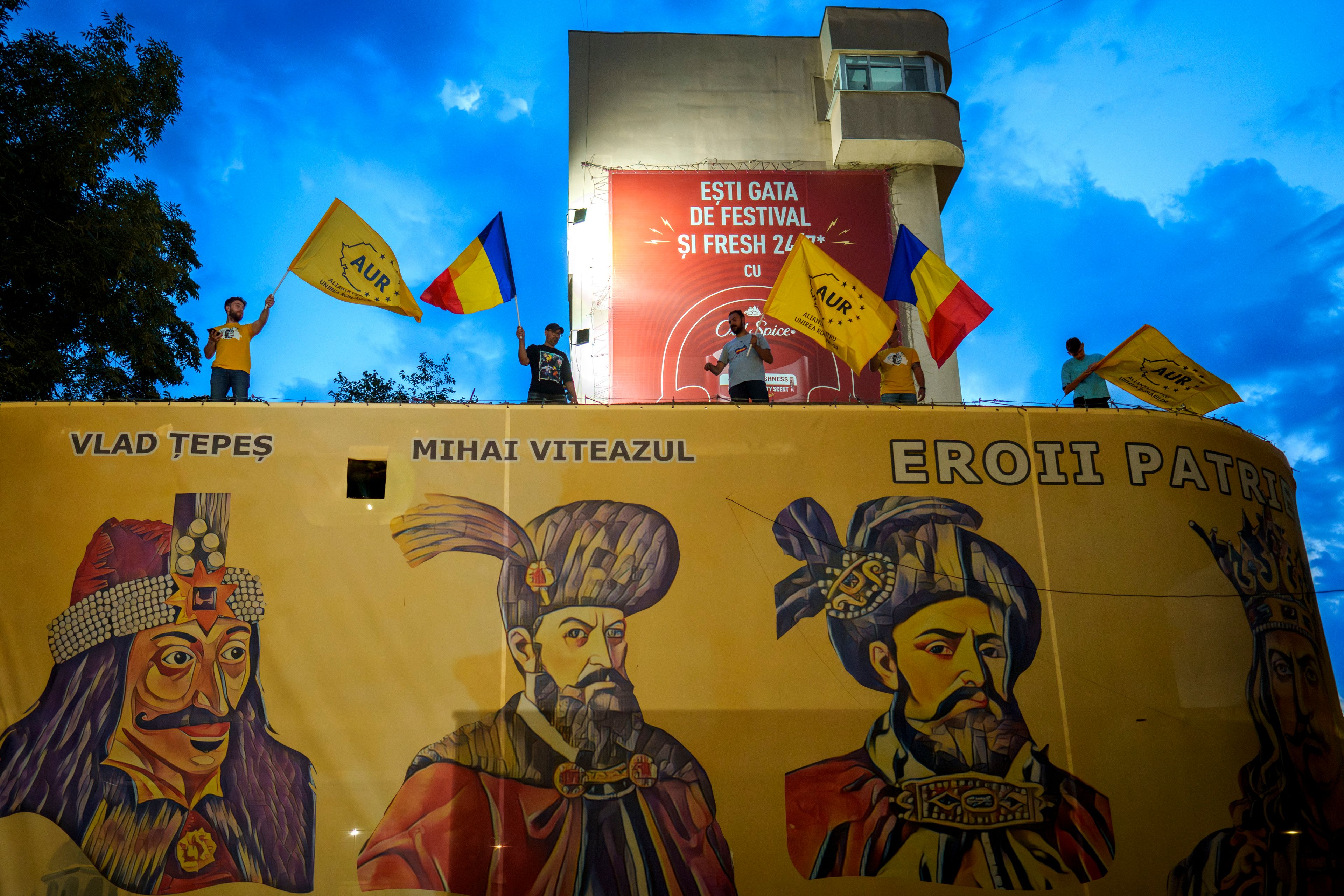 Supporters of the right wing party Alliance for the Unification of Romanians (AUR) wave flags standing above a large poster depicting medieval Romanian rulers, outside the party headquarters, before the announcement of exit polls in European elections in Bucharest, Romania, Sunday, June 9, 2024.