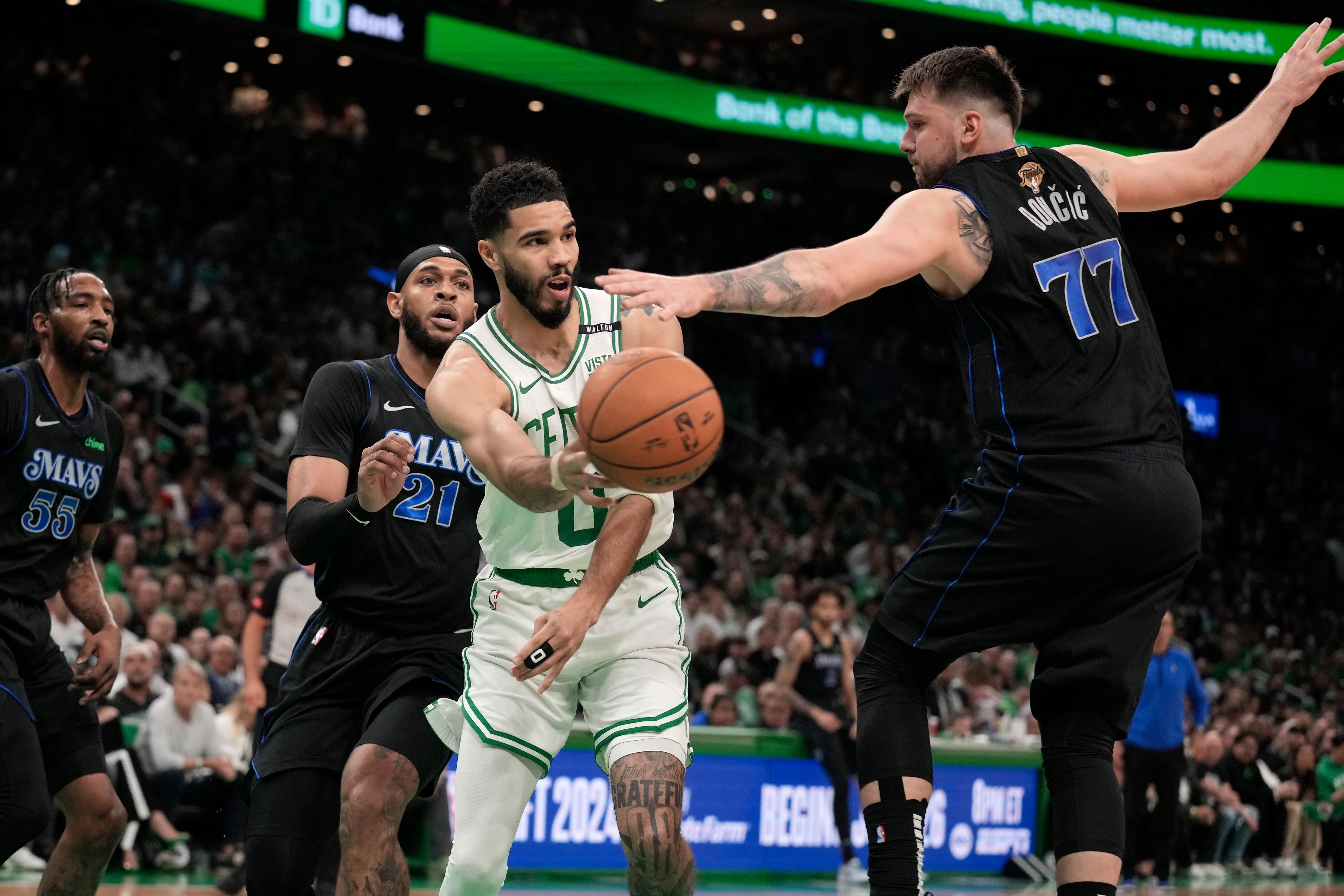 Boston Celtics forward Jayson Tatum (0) passes the ball around Dallas Mavericks guard Luka Doncic (77) as forward Derrick Jones Jr. (55) and center Daniel Gafford (21) defend during the first half of Game 1 of basketball's NBA Finals on Thursday, June 6, 2024, in Boston.