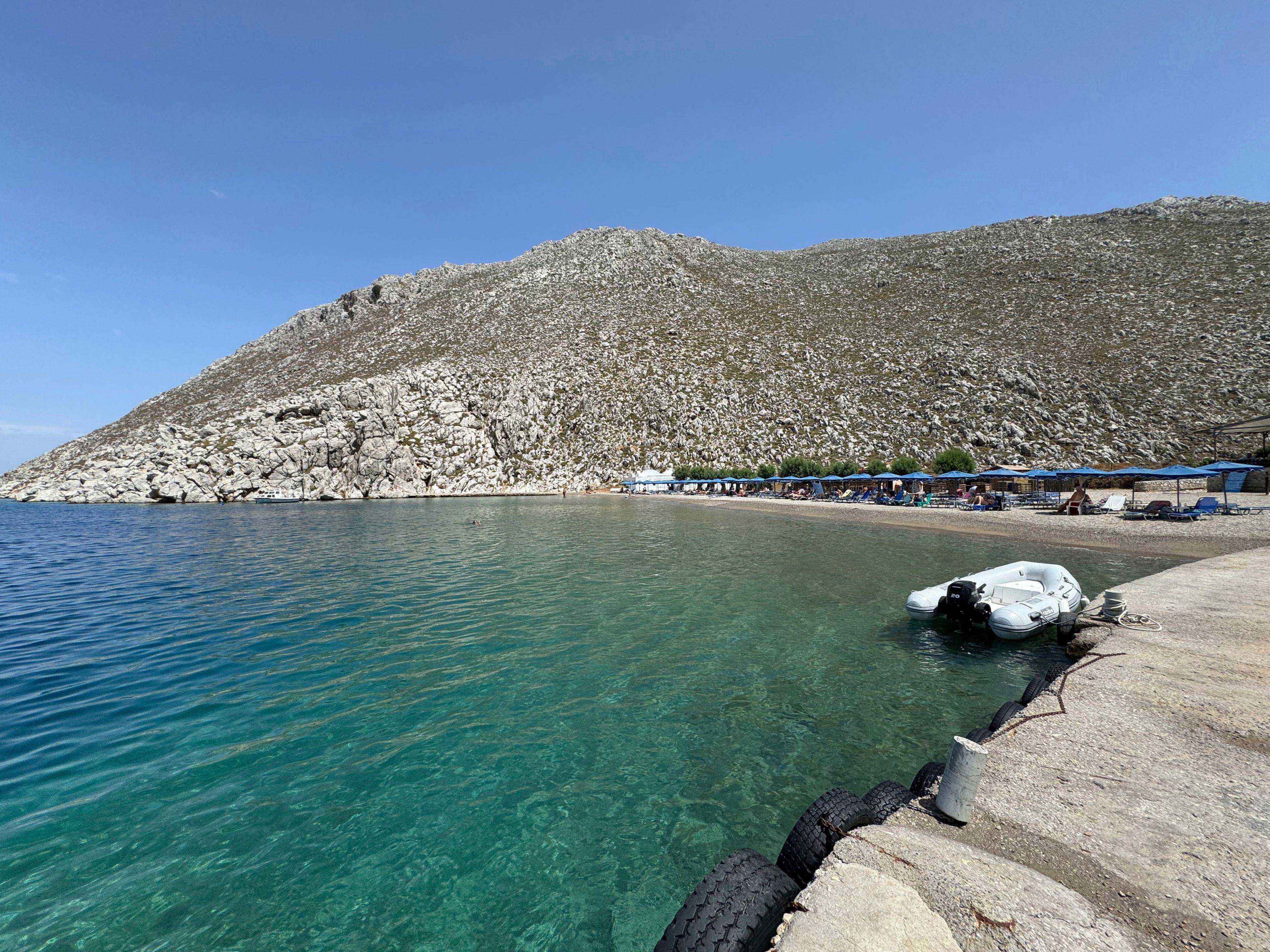 People sit on the beach of Agios Nikolaos from where British doctor and television presenter Michael Mosley, is believed to have set out, on the southeastern Aegean Sea island of Symi, Greece, Friday, June 7, 2024. Greek police say an ongoing major search and rescue operation on the small eastern Aegean island of Symi has still not located British doctor and television presenter Michael Mosley, who went missing on Wednesday afternoon after reportedly going for a walk.