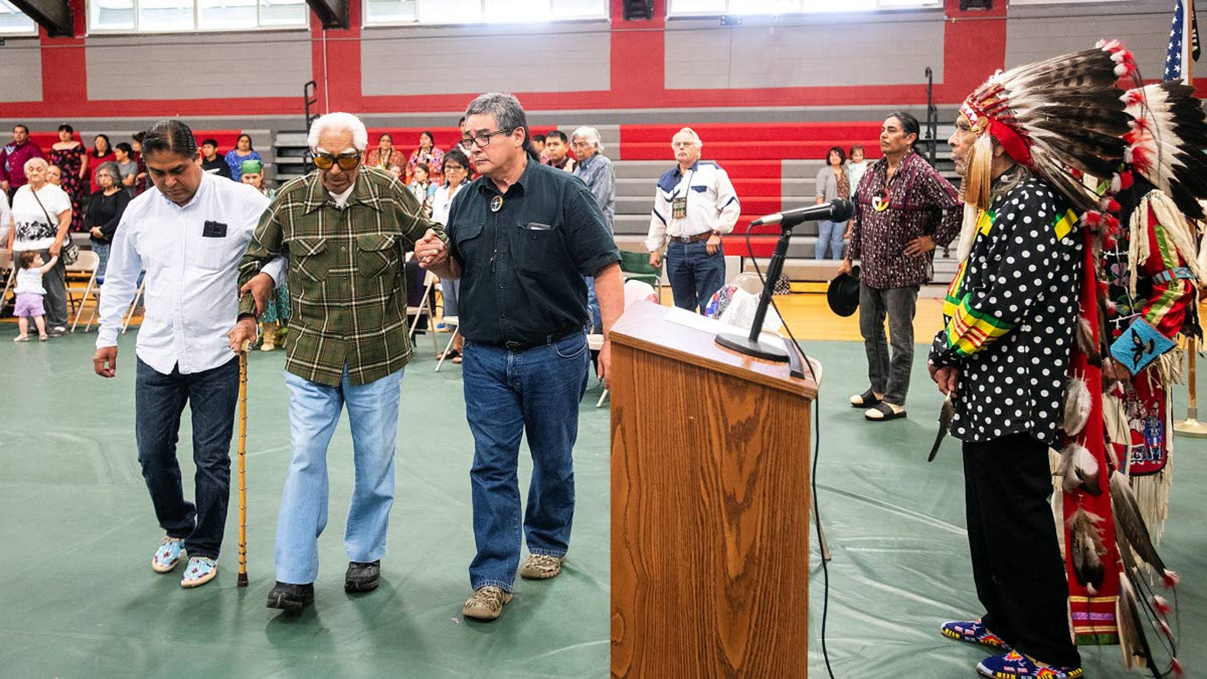 With the aid of family members, Alex Pinkham Jr., 94, walks amidst a gym of standing admirers as he is honored for his service in World War II during a ceremony Saturday afternoon at the Pi-Nee-Waus Community Center in Lapwai.