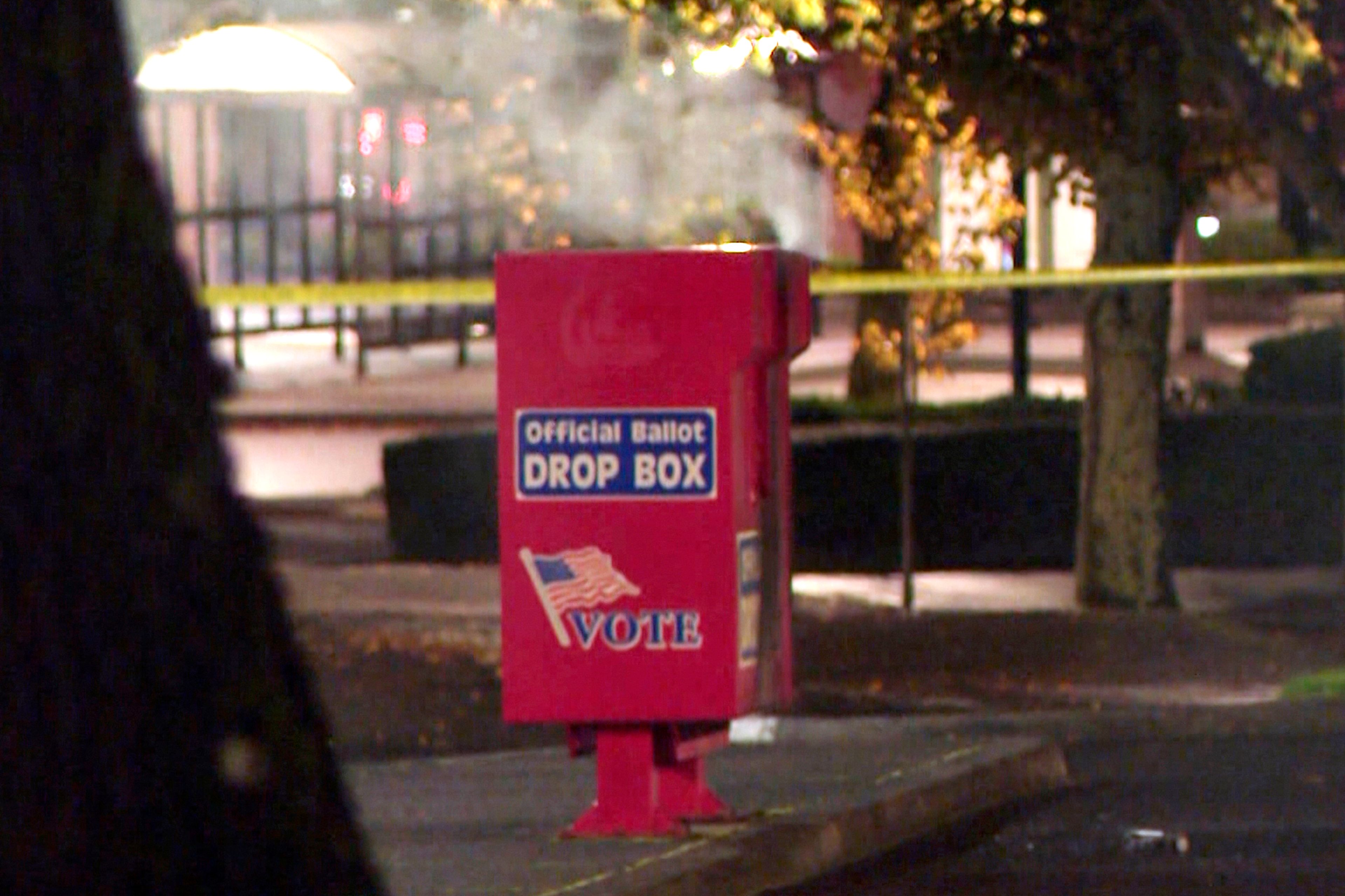 In this image made from a video provided by KGW8, authorities investigate the scene as smoke pours out of a ballot box on Monday, Oct. 28, 2024, in Vancouver, Wash. (KGW8 via AP)