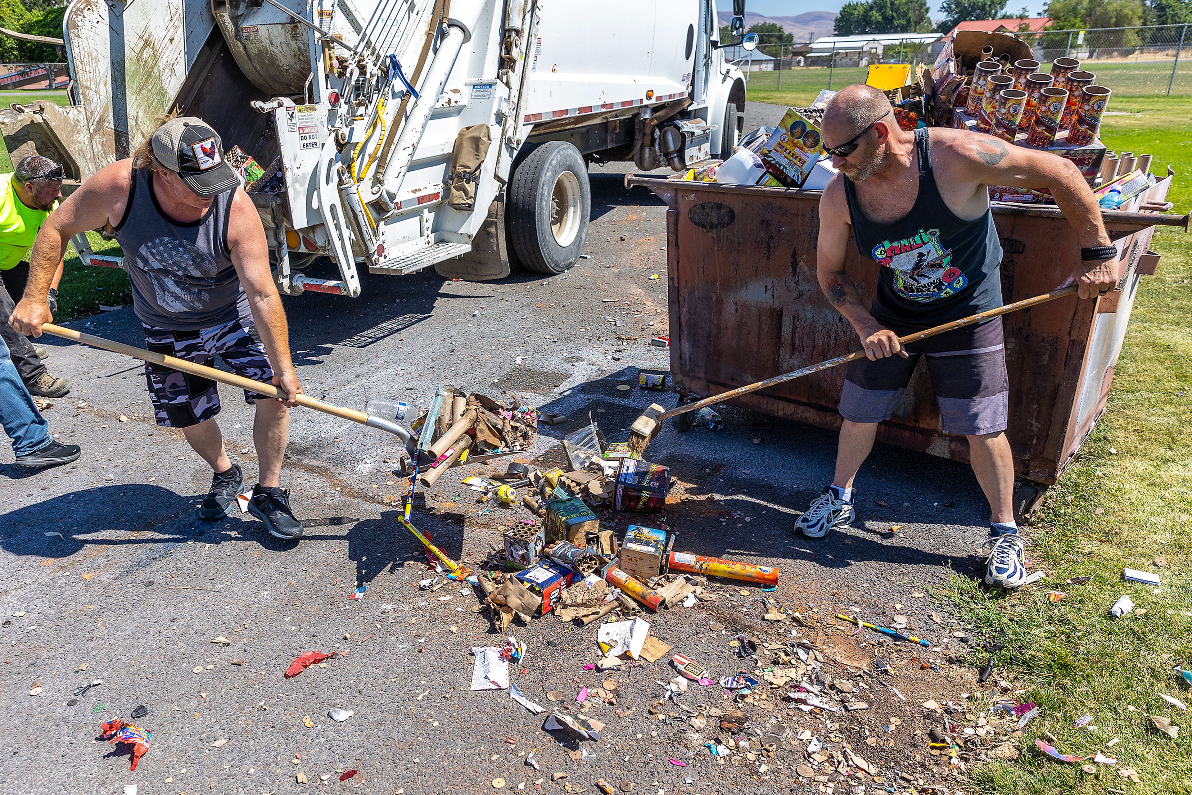 Kris Dugger, left, and Bill Horton sweep up firework debris before throwing it in a garbage truck Friday in the fields behind Lincoln Middle School. The two arrived early after 8 a.m. to collect the trash into piles.