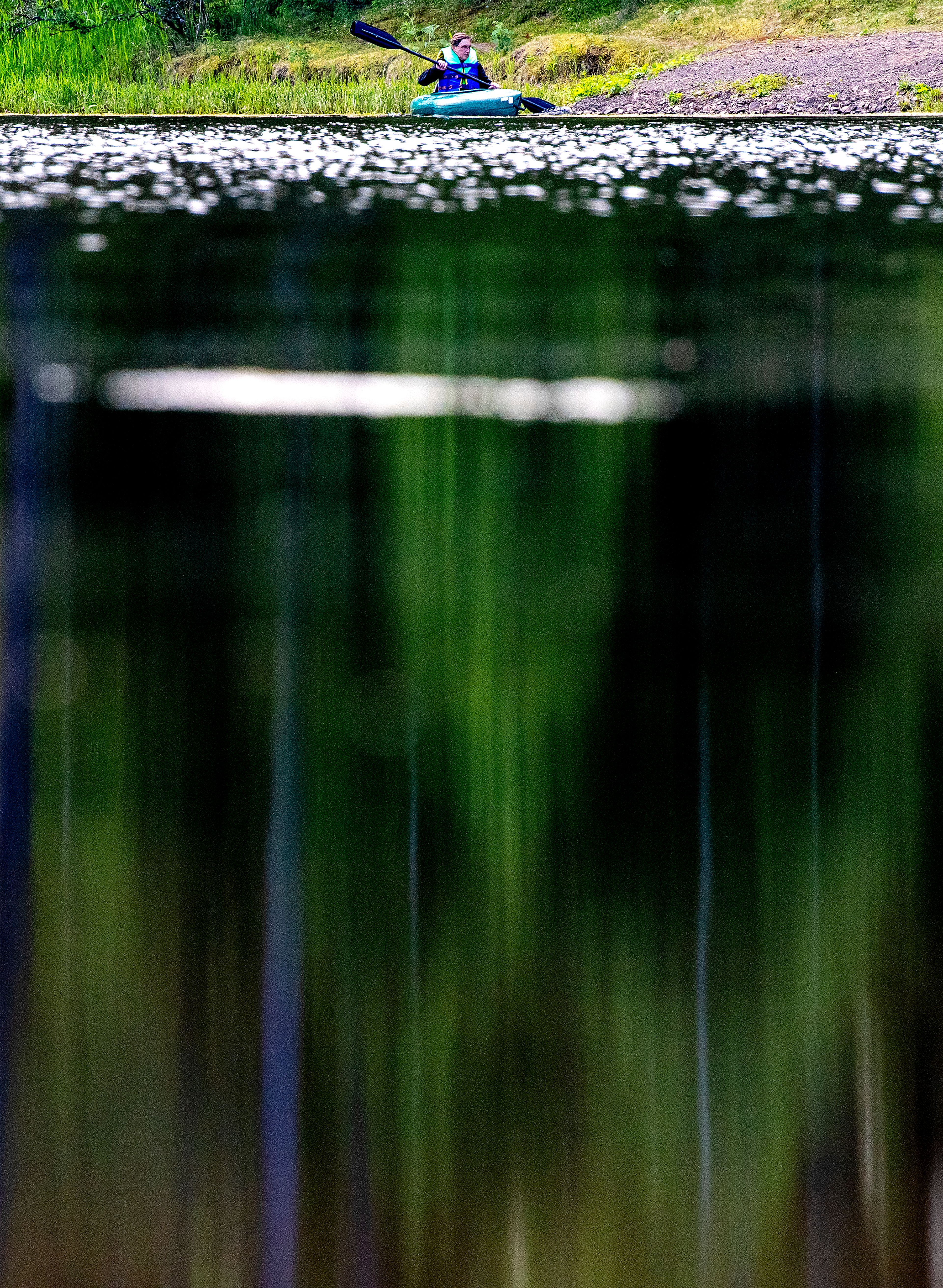 A kayaker paddles toward shore at Winchester Lake in July of 2021, as trees are reflected against the water's surface.