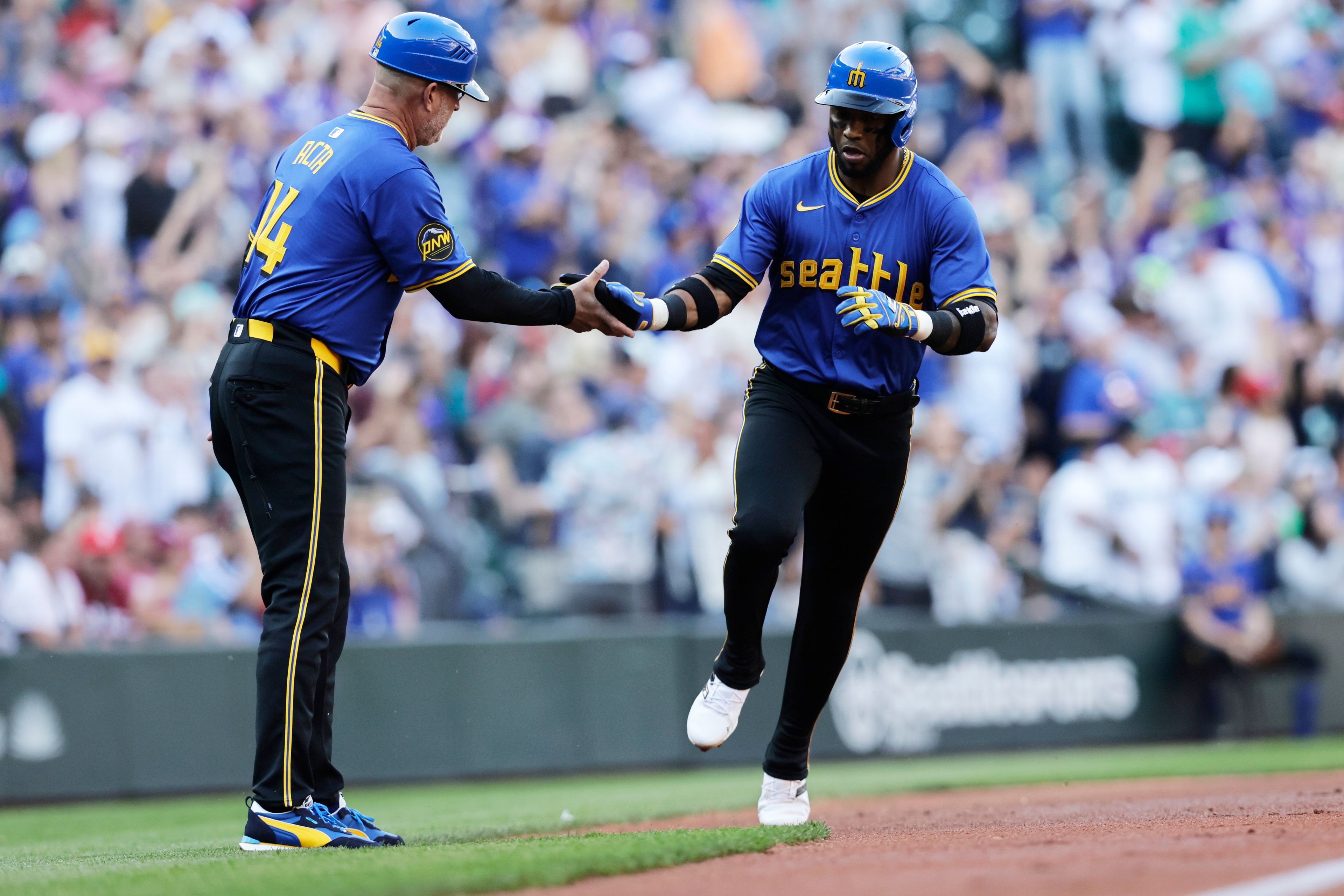 Seattle Mariners center fielder Victor Robles, right, is greeted by third base coach Manny Acta on his solo home run off Philadelphia Phillies starting pitcher Tyler Phillips during the first inning in a baseball game, Friday, Aug. 2, 2024, in Seattle. (AP Photo/John Froschauer)