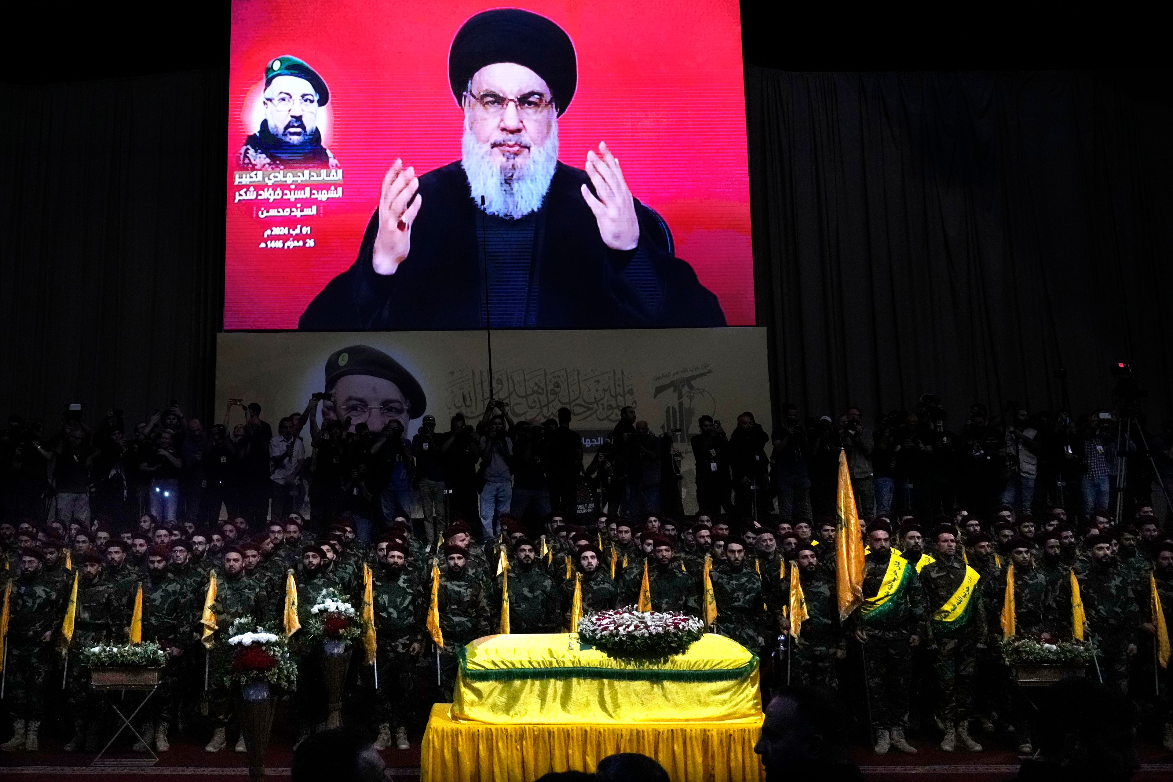 FILE - Hezbollah fighters stand behind the coffin of their top commander Fouad Shukur, who was killed by an Israeli airstrike on July 30, as Hezbollah leader Sayyed Hassan Nasrallah speaks through a screen during Shukur's funeral in a southern suburb of Beirut, Lebanon, Aug. 1, 2024. (AP Photo/Hussein Malla, File)