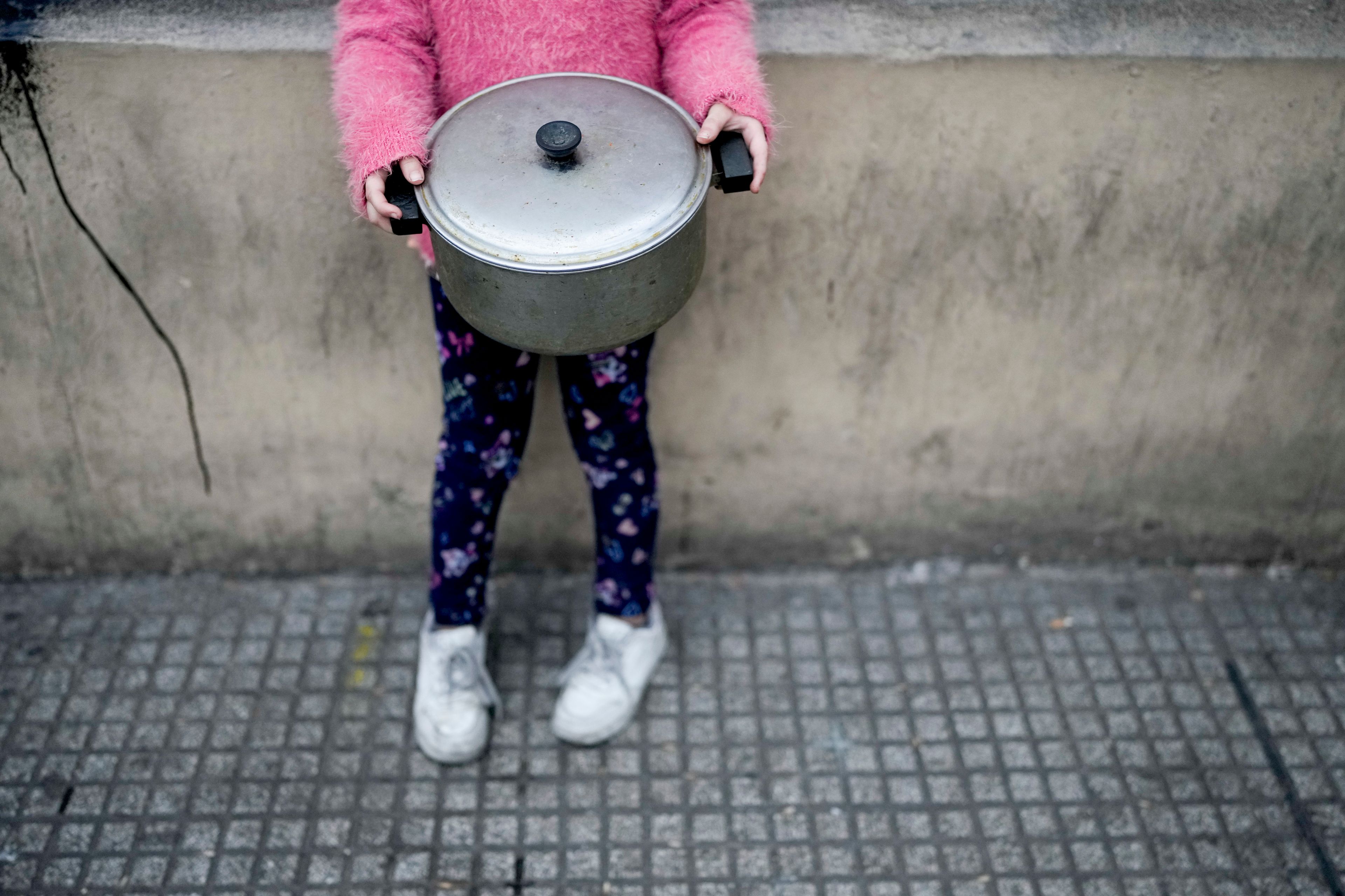 A little girl clutches her pot outside a soup kitchen where she waits in line for her turn to collect a free, cooked meal to take home in Buenos Aires, Argentina, Monday, Sept. 9, 2024. (AP Photo/Natacha Pisarenko)