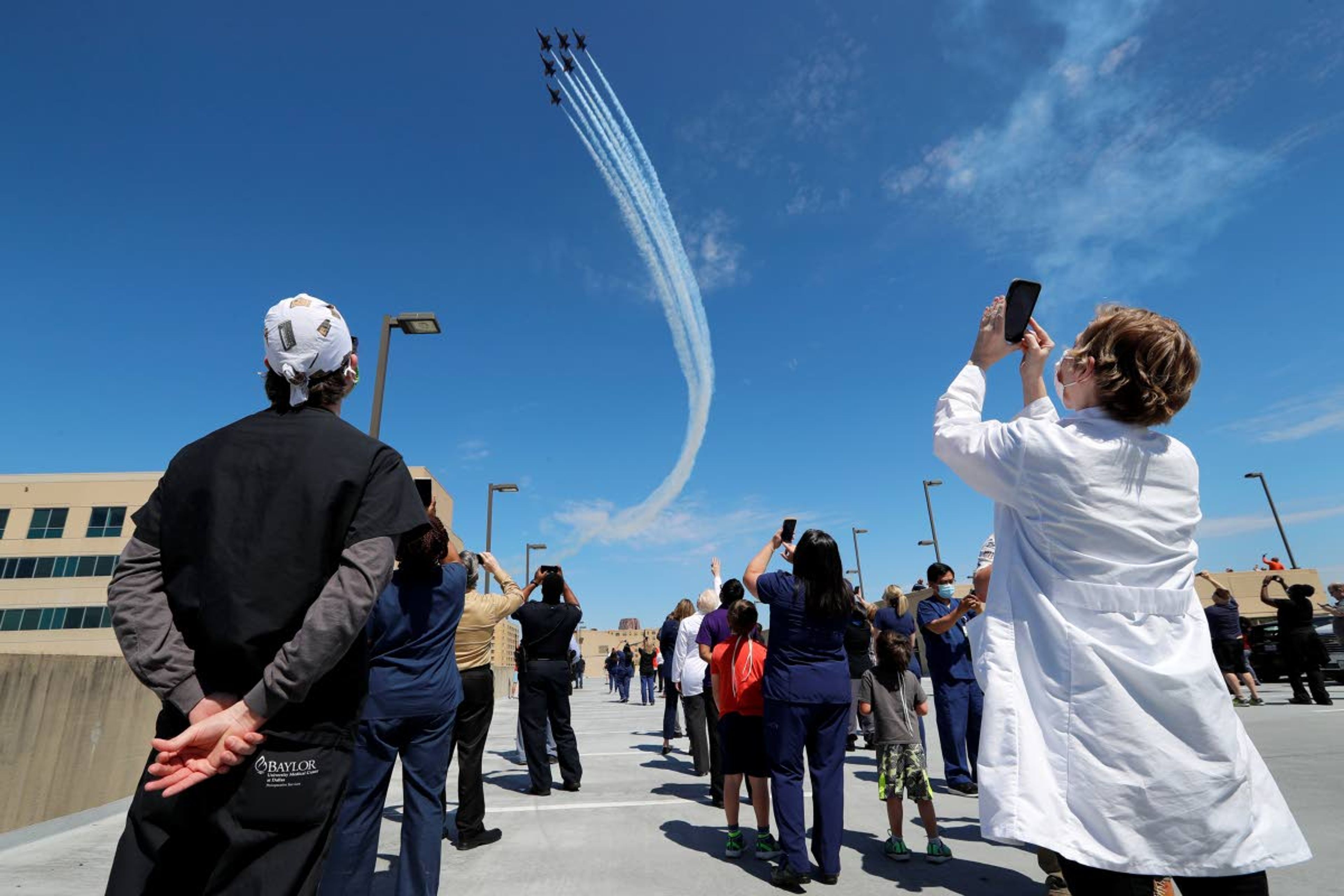 Nathan Golub, left, Operations Manager of Surgical Services and Angela Wilson, Coordinator of Transplant Programs at Baylor Scott & White Hospital watch as the U.S. Navy Blue Angels fly over their hospital in Dallas, Wednesday, May 6, 2020. (AP Photo/Tony Gutierrez)