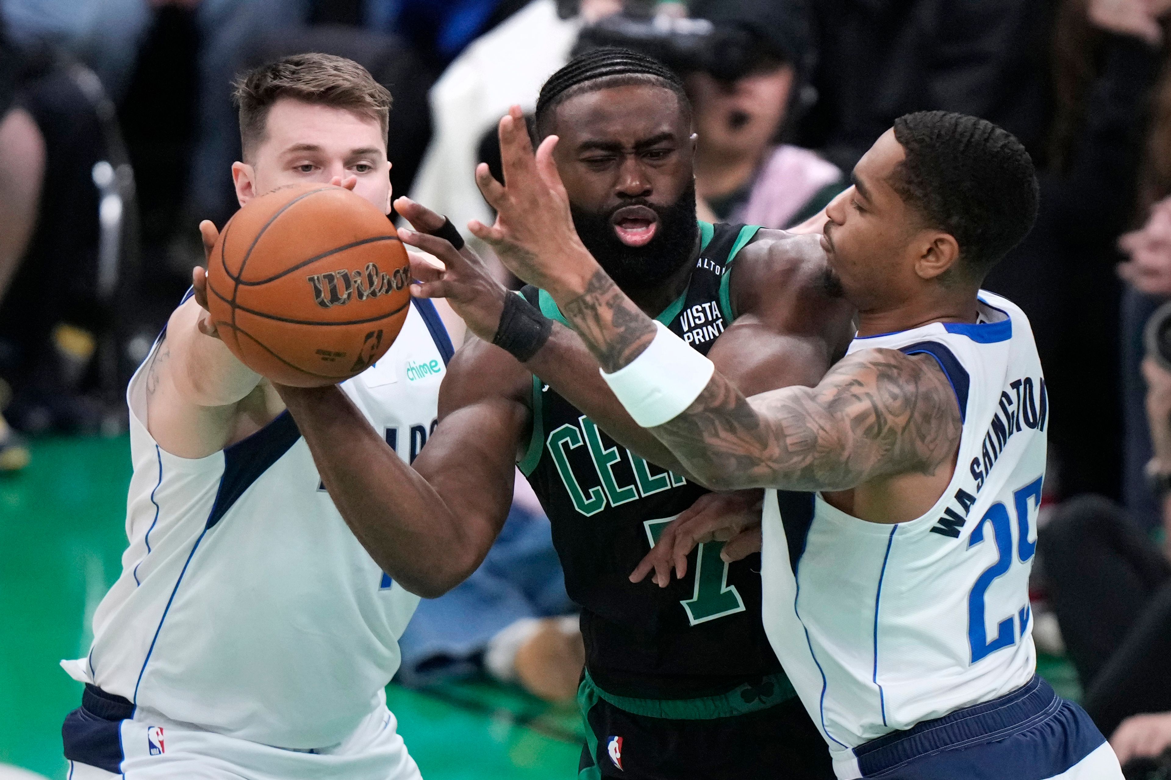 Boston Celtics guard Jaylen Brown, center, tries to pass while pressured by Dallas Mavericks forward P.J. Washington (25) and guard Luka Doncic, left, during the first half of Game 2 of the NBA Finals basketball series, Sunday, June 9, 2024, in Boston.