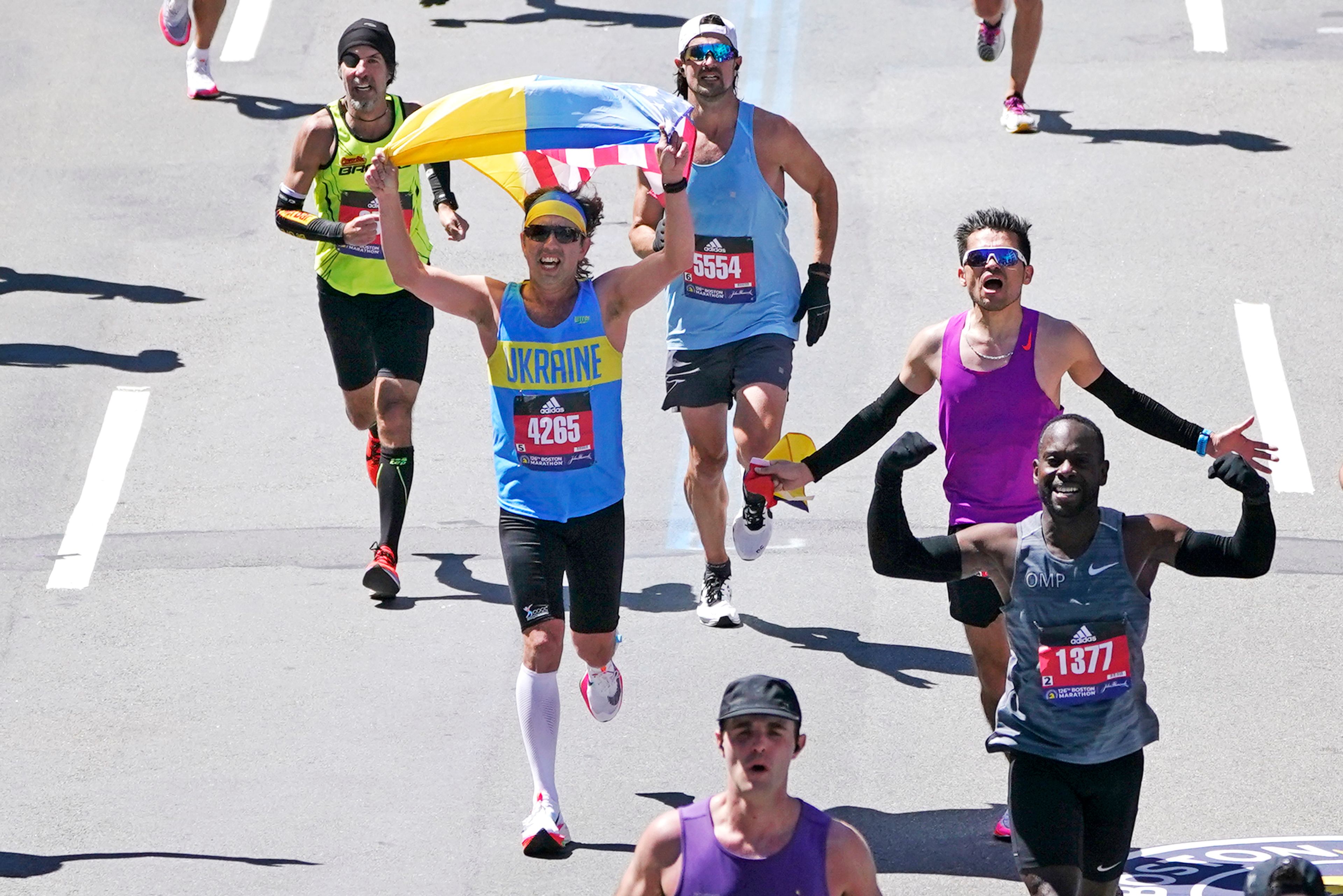 While dressed in a Ukraine shirt, a runner holds a Ukraine and American flag while approaching the finish line Monday in Boston.