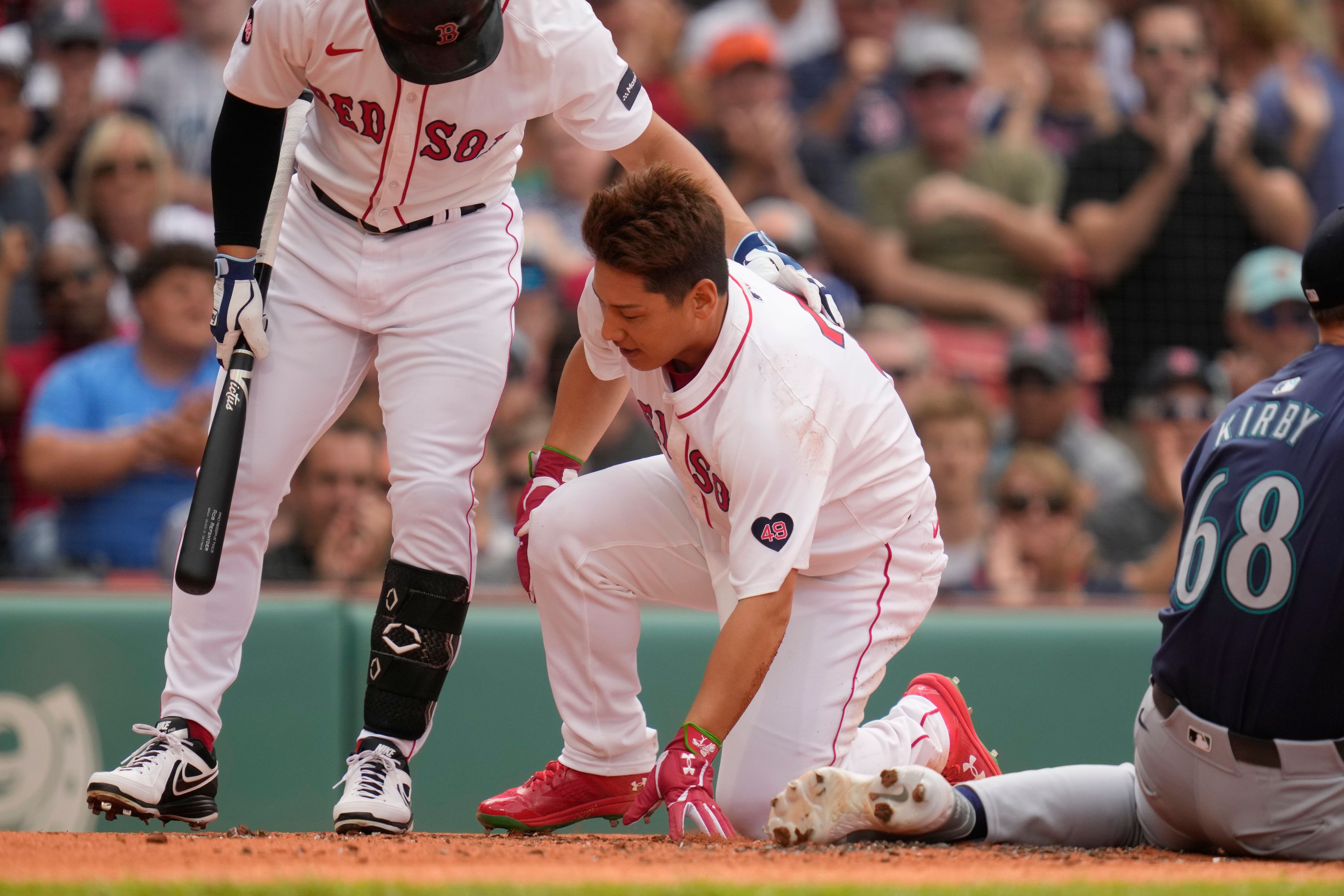 Boston Red Sox's Masataka Yoshida, right, is helped by teammate Rob Refsnyder after colliding with Seattle Mariners pitcher George Kirby, while scoring on a wild pitch during the first inning of a baseball game, Wednesday, July 31, 2024, in Boston. (AP Photo/Charles Krupa)