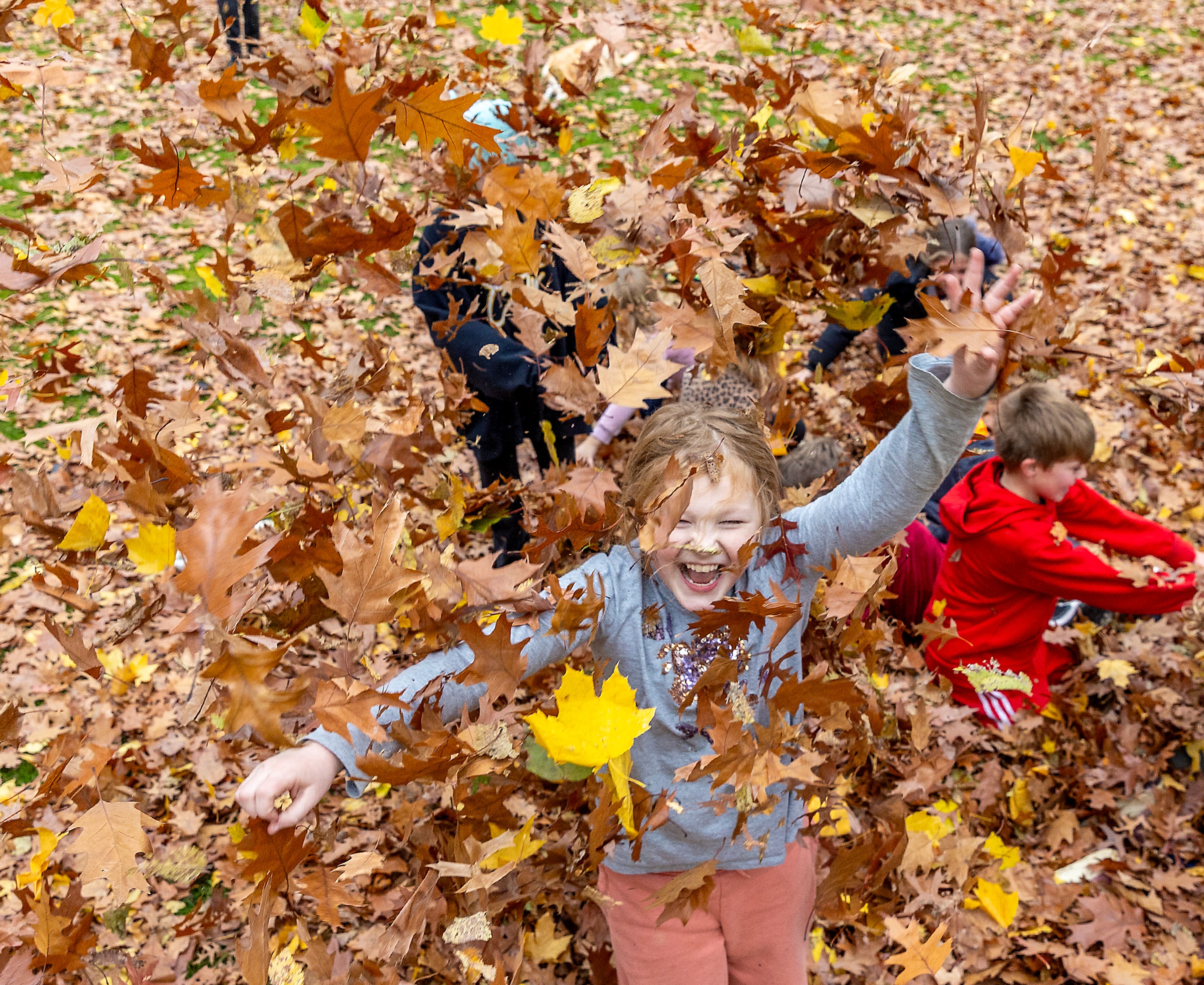 Maya Pearson lets leaves fall down around her Wednesday outside Children's House Montessori School at Pioneer Park Wednesday in Lewiston.