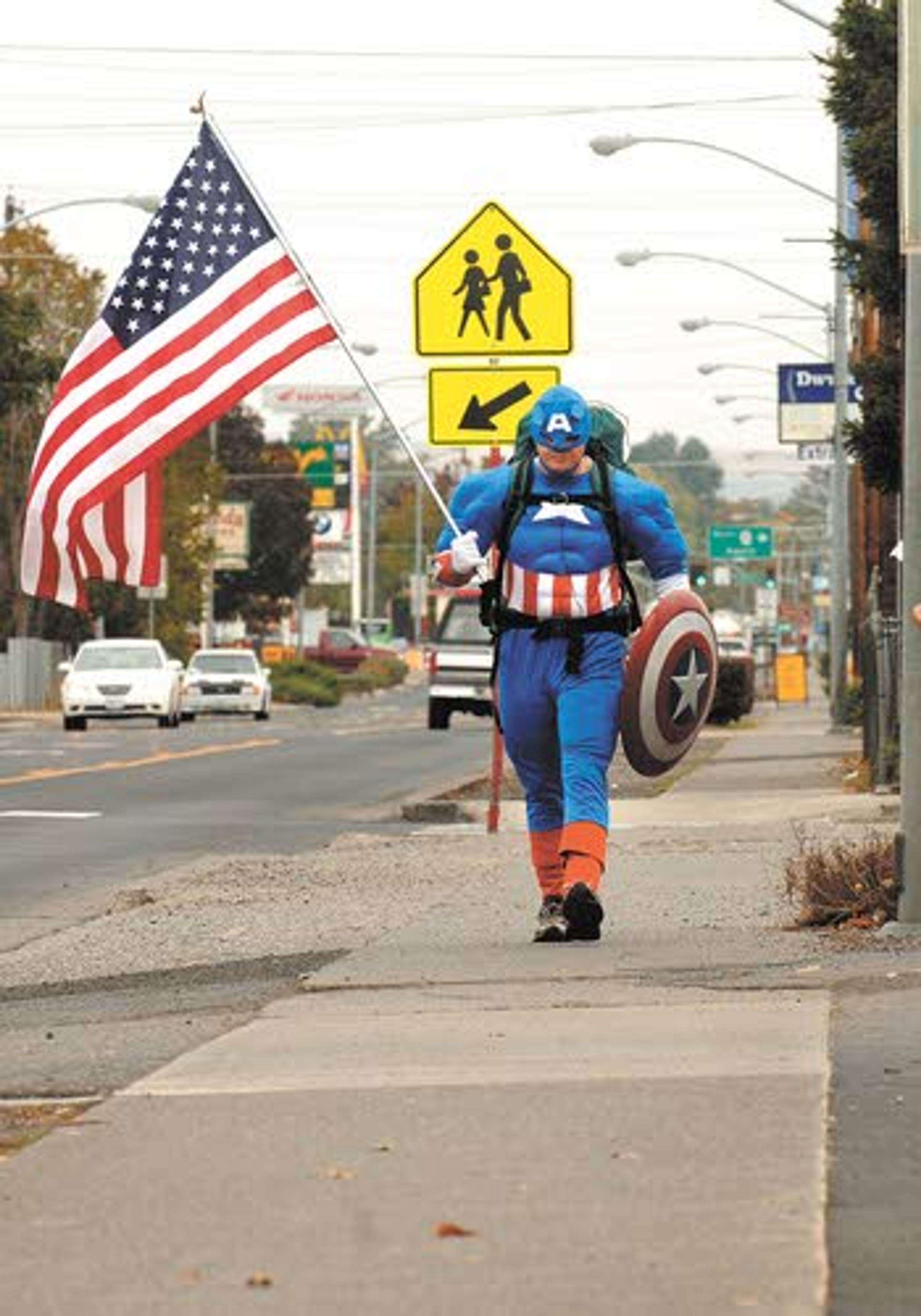 Wearing a Captain America suit, Allen Mullins of Dalton, Ga.,
walks down Bridge Street as he makes his way through Clarkston
Friday on his way to Olympia. Mullins is visiting every state
capital as he walks across America to bring awareness to U.S.
military veterans.