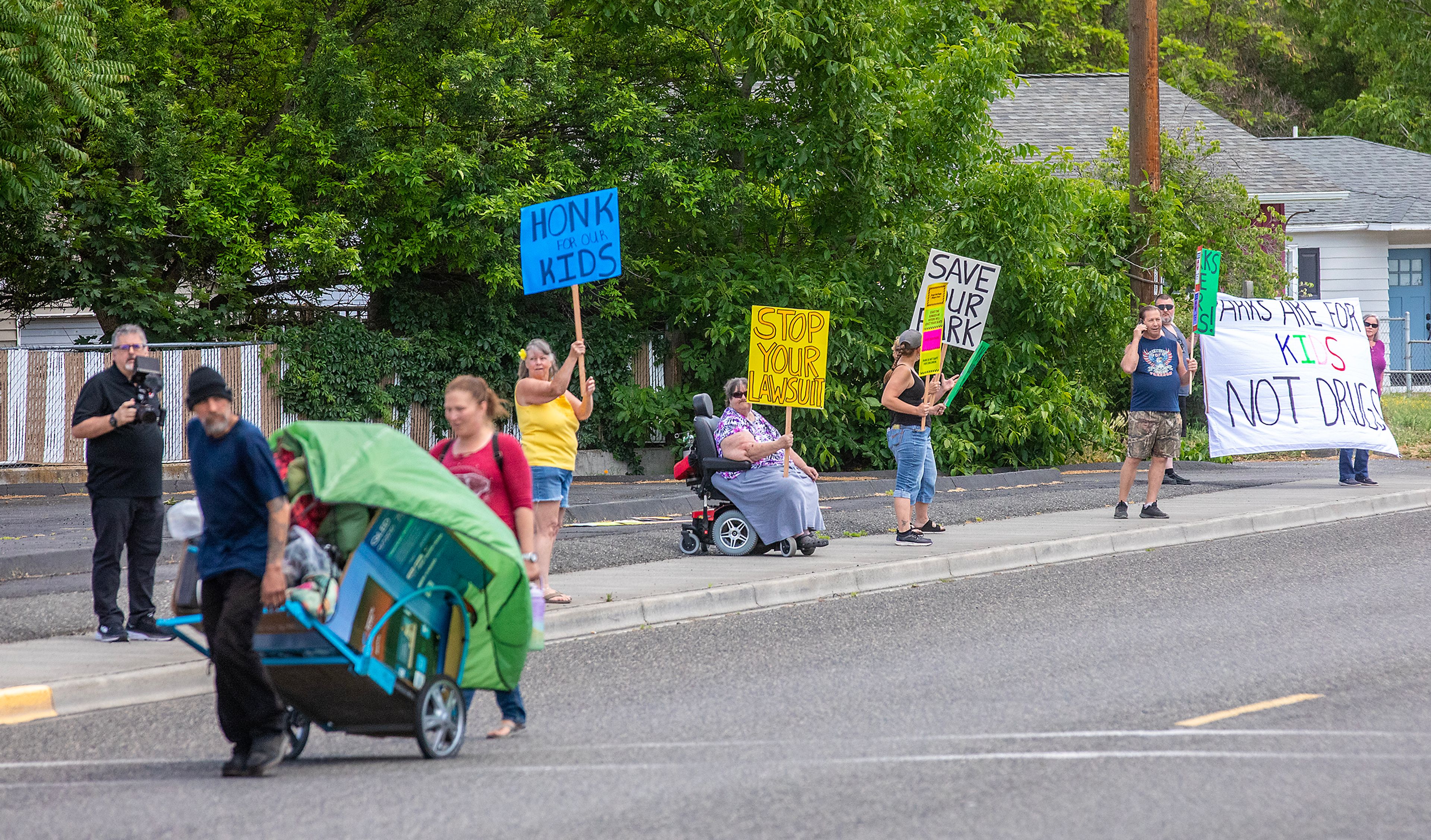 Protesters in opposition to homeless camping at Foster Park stand along Diagonal Street nearby Foster Park as a person crosses the street during the Elves for the Homeless event “Summer of Kindness” Wednesday in Clarkston.