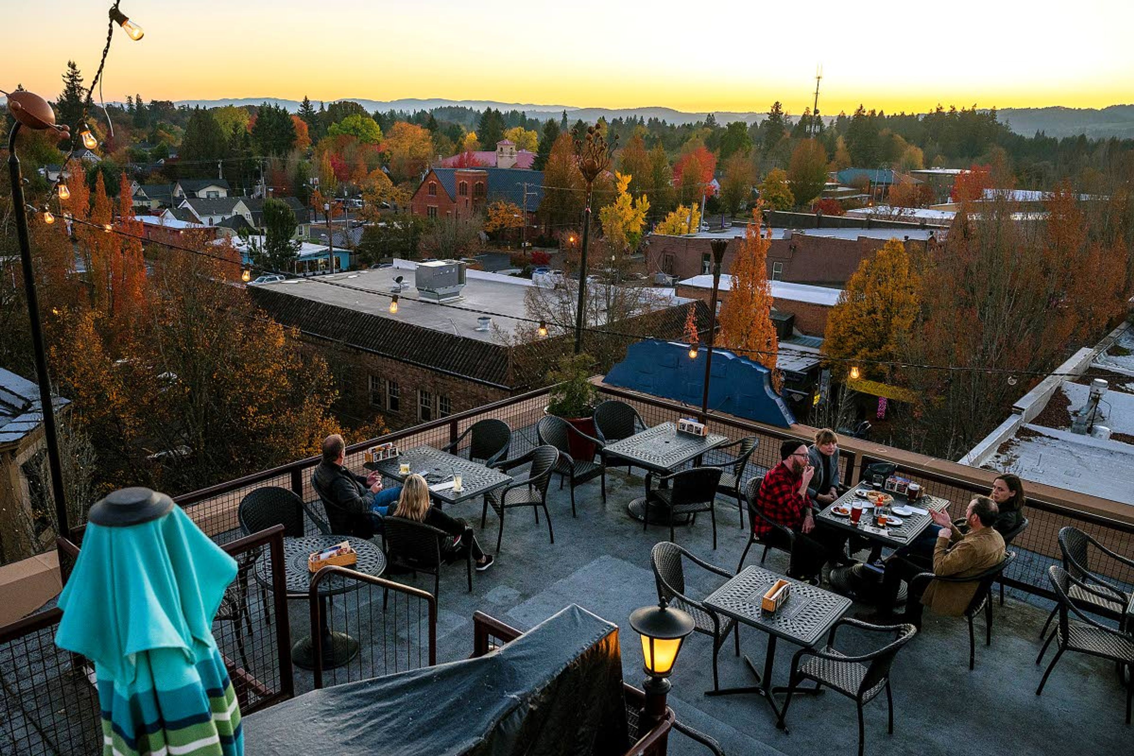 The sun sets behind the colorful trees and hills west of McMinnville, Ore., as people enjoy a pleasant evening on the rooftop bar at McMenamins Hotel Oregon on Third Street in downtown McMinnville.