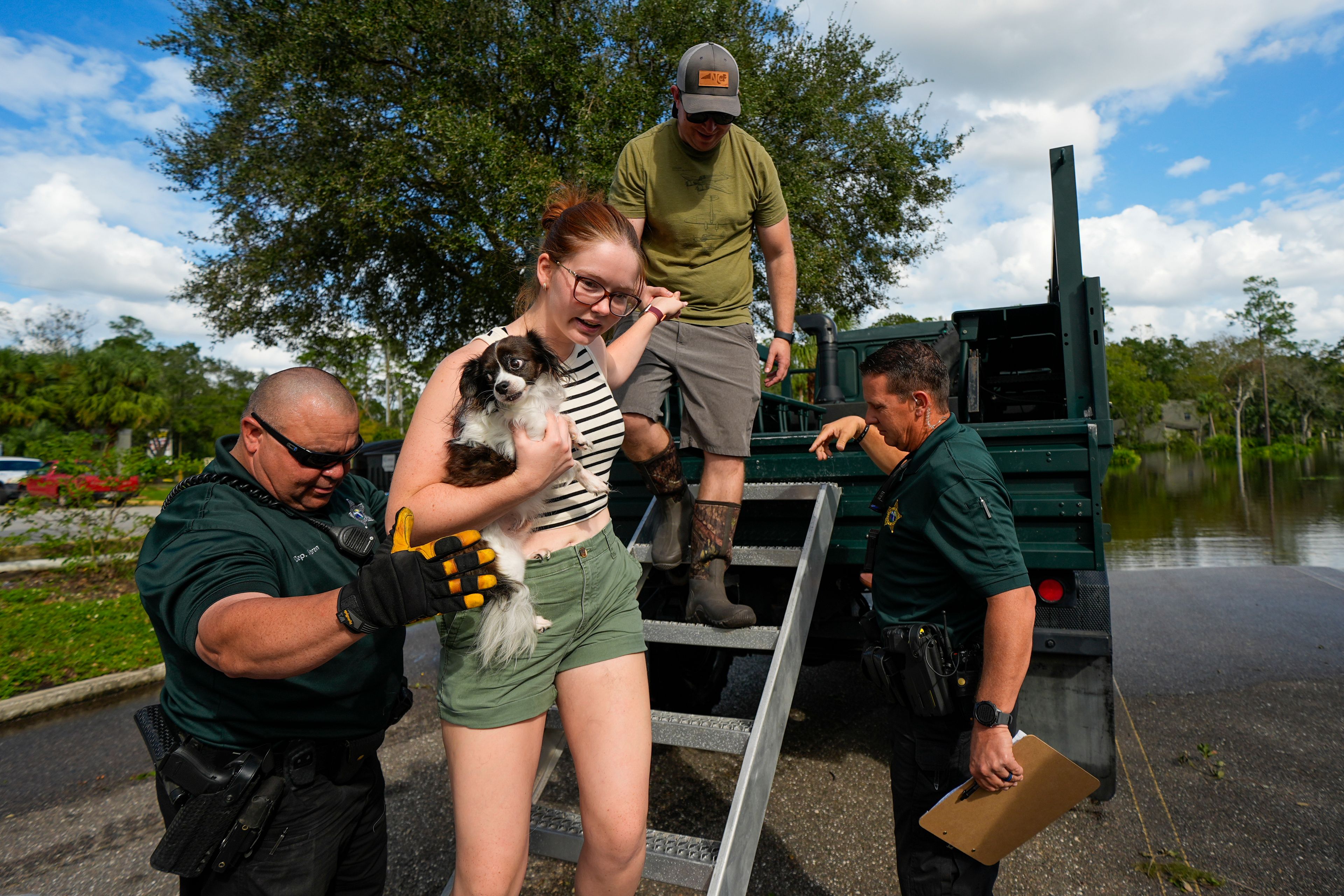 Sarah McRee holds a dog named Poe as she is helped off a high-clearance vehicle by Panellas County Sheriff officials after she was escorted in and out of the Tarpon Woods neighborhood as people return to their homes following Hurricane Milton, Friday, Oct. 11, 2024, in Palm Harbor, Fla. (AP Photo/Julio Cortez)