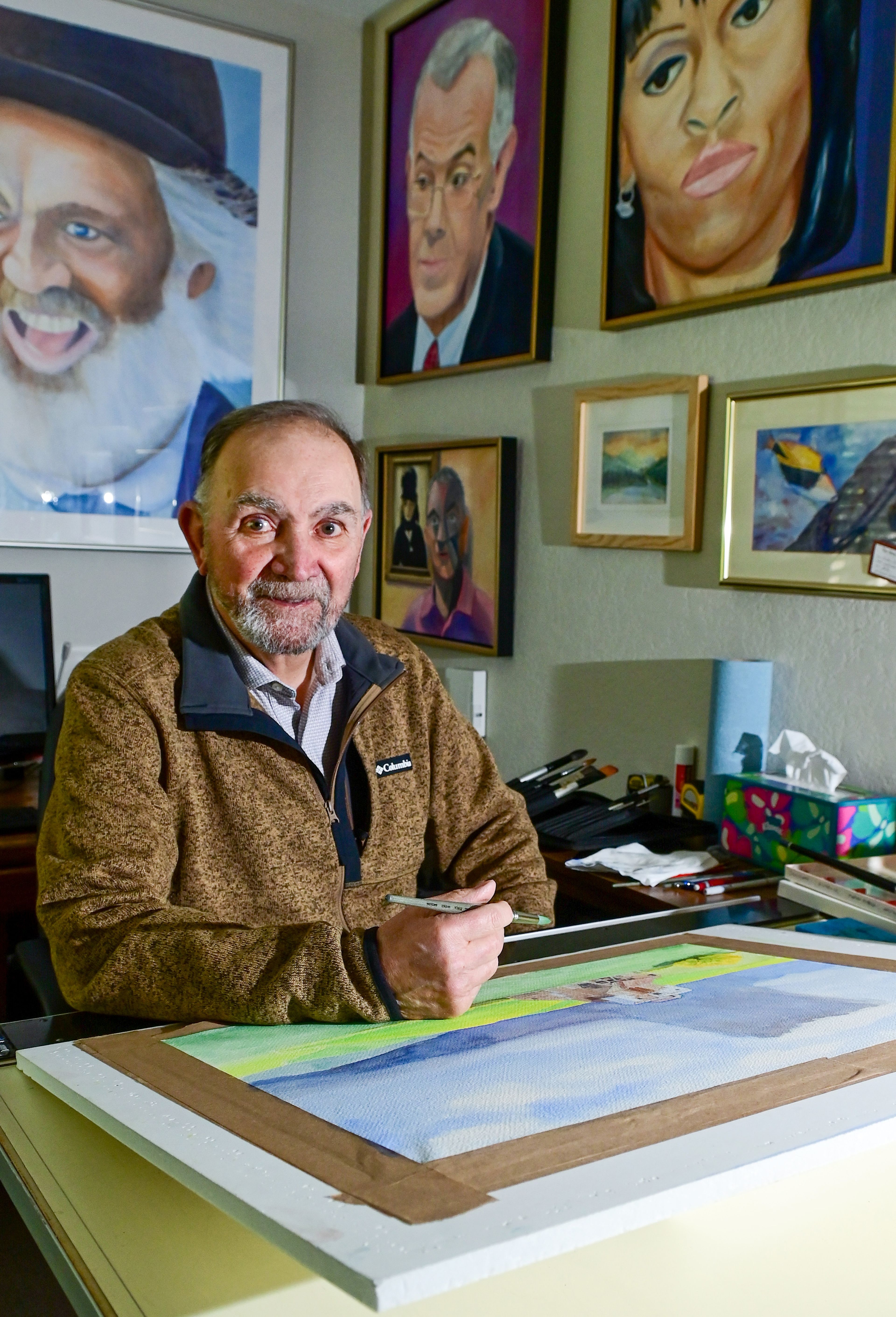 Ernie Weiss, president of the Palouse Watercolor Socius, sits in front of an in-progress watercolor piece, named “Abandoned,” that will be entered in the 50th anniversary show for the group. Other artwork by Weiss hangs on the walls around him.