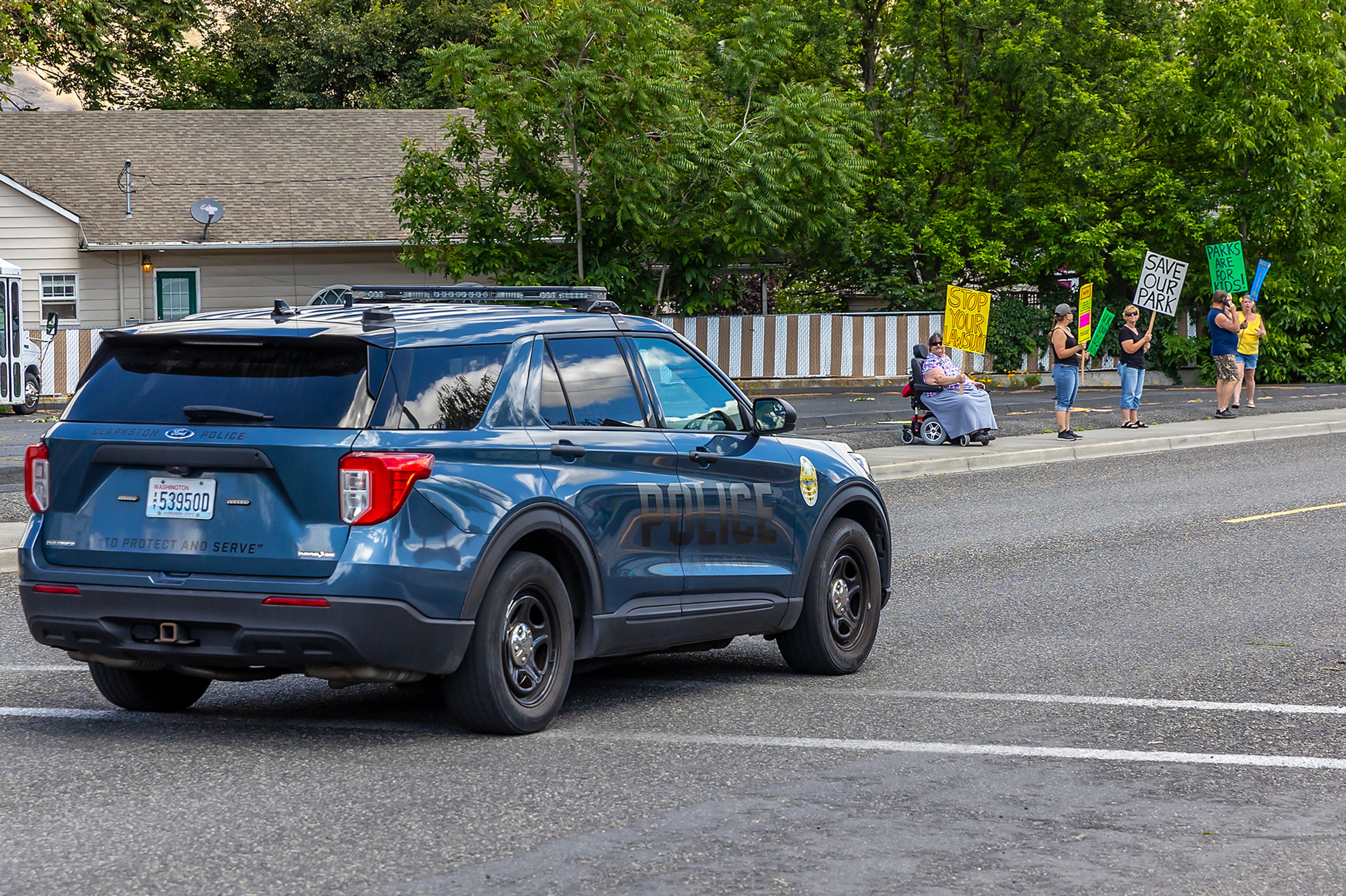 A Clarkston police vehicle drives past people protesting the presence of homeless people at Foster Park Wednesday in Clarkston.