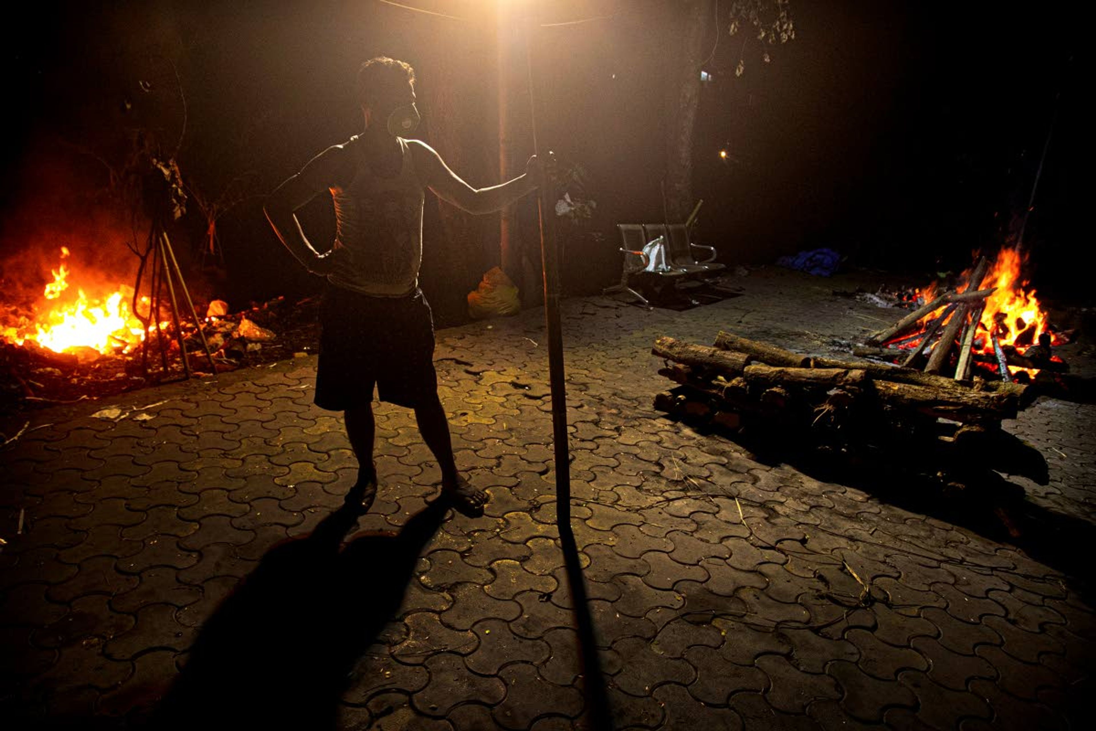 Ramananda Sarkar, 43, stands by burning funeral pyres of COVID-19 victims in Gauhati, India, Monday, Sept. 14, 2020. While Hindu's believe cremation rights are sacred and release the dead person's soul from the cycle of rebirth, those who actually deal with corpses are looked down upon. With a mask on his face and a prayer on his lips, he cremates bodies brought in by a handful of relatives in protective suits, hurried affairs conducted with minimal rituals under the state government’s guidelines. Sarkar said he alone has cremated more than 450 COVID-19 victims. (AP Photo/Anupam Nath)