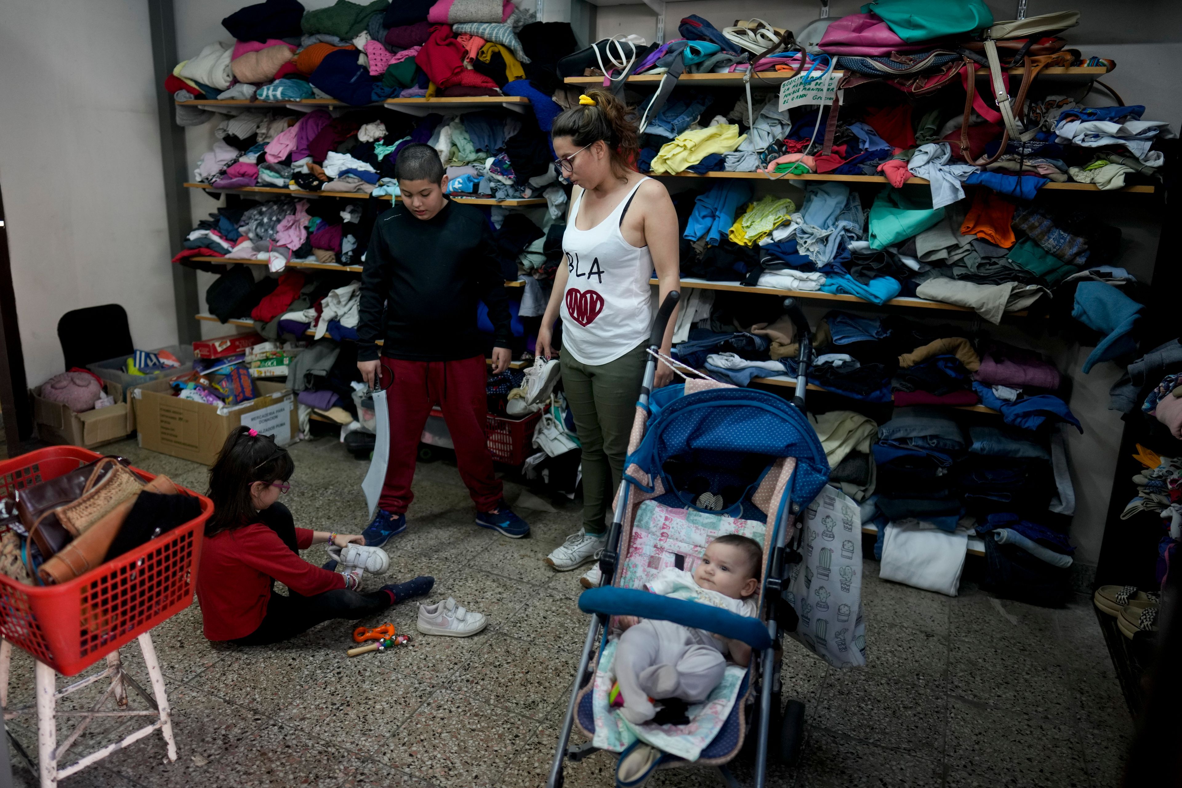 Rocio Costa watches her daughter Francesca try on shoes at a second-hand clothing fair alongside her other children Almendra and Tiziano in Buenos Aires, Argentina, Monday, Sept. 16, 2024. (AP Photo/Natacha Pisarenko)