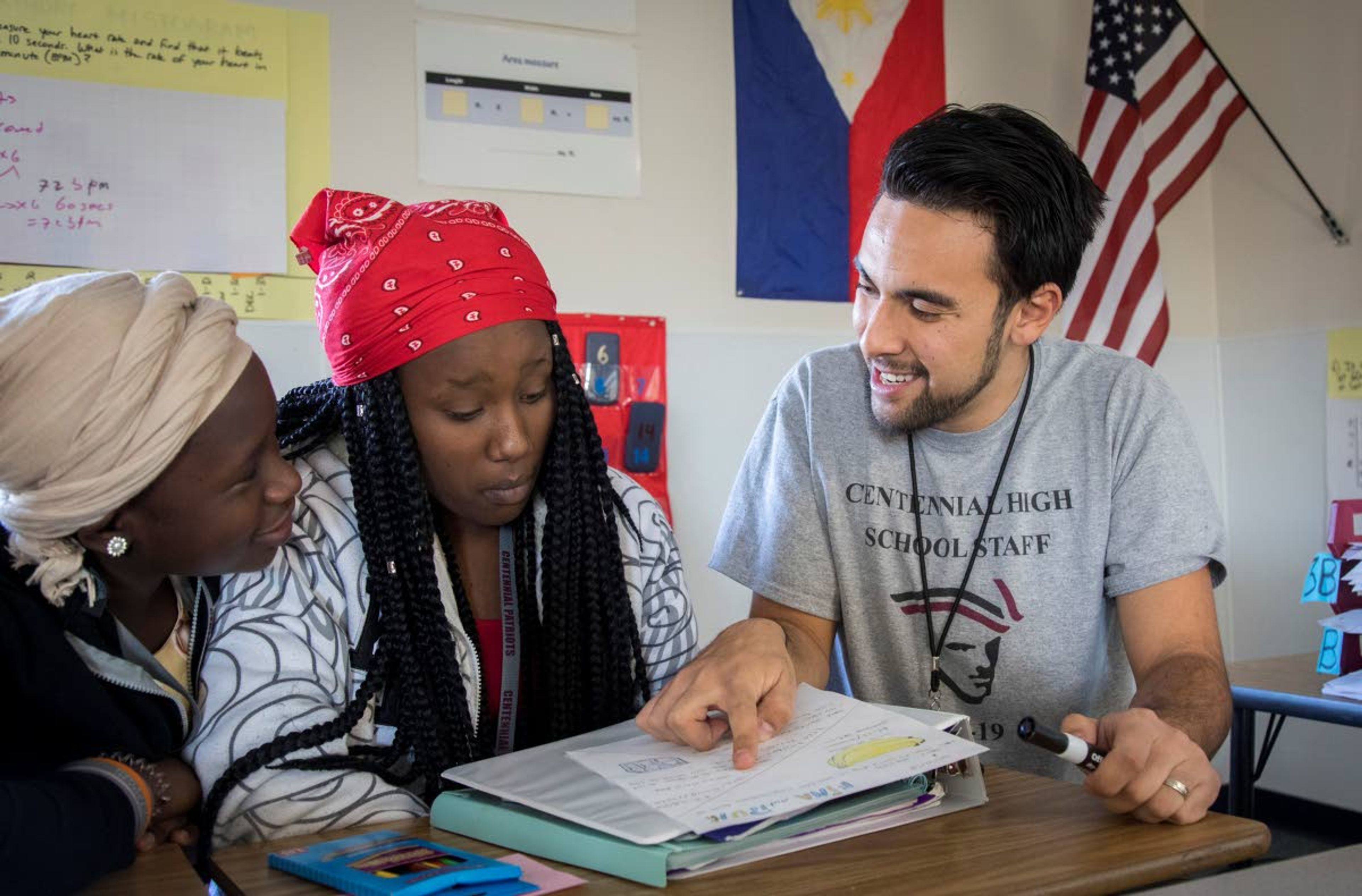 Faris works with Rina Urayeneza, center, whose family is from Rwanda, and Ruth Gakuru, from Congo, going over the prices in their grocery store as they learn consumer language and prices per unit at Centennial High School in Boise, Idaho. Faris, 25, is a math teacher in Centennial High School's English as a New Language department. He helps refugee kids, ages 14 to 20 years old, learn math — and English — through immersion in reading, writing, speaking and listening.