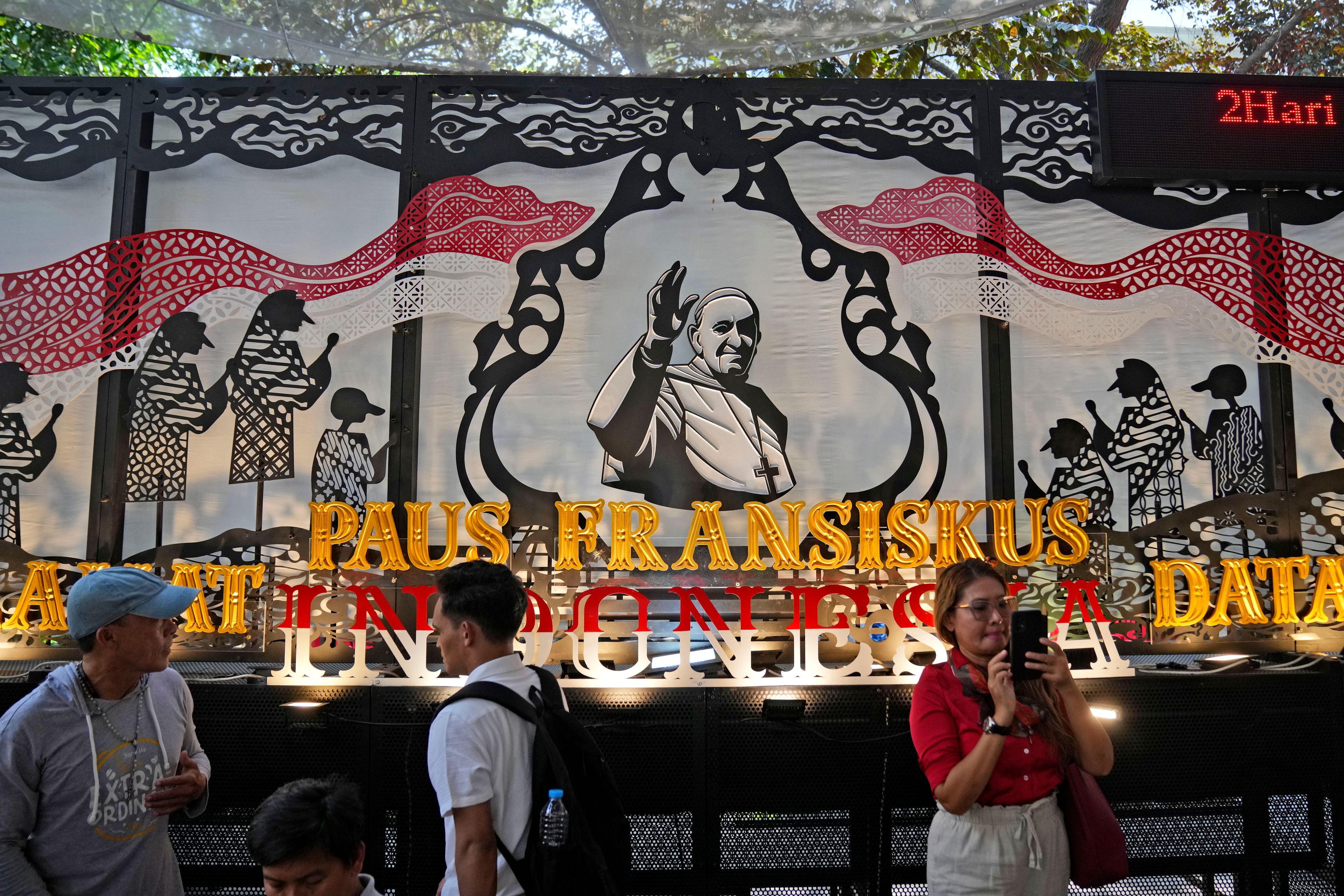 People walk past a welcoming signboard for Pope Francis displayed at Jakarta Cathedral in Jakarta, Indonesia, Sunday, Sept. 1, 2024, ahead of his visit to Indonesia from Sept. 3-6.