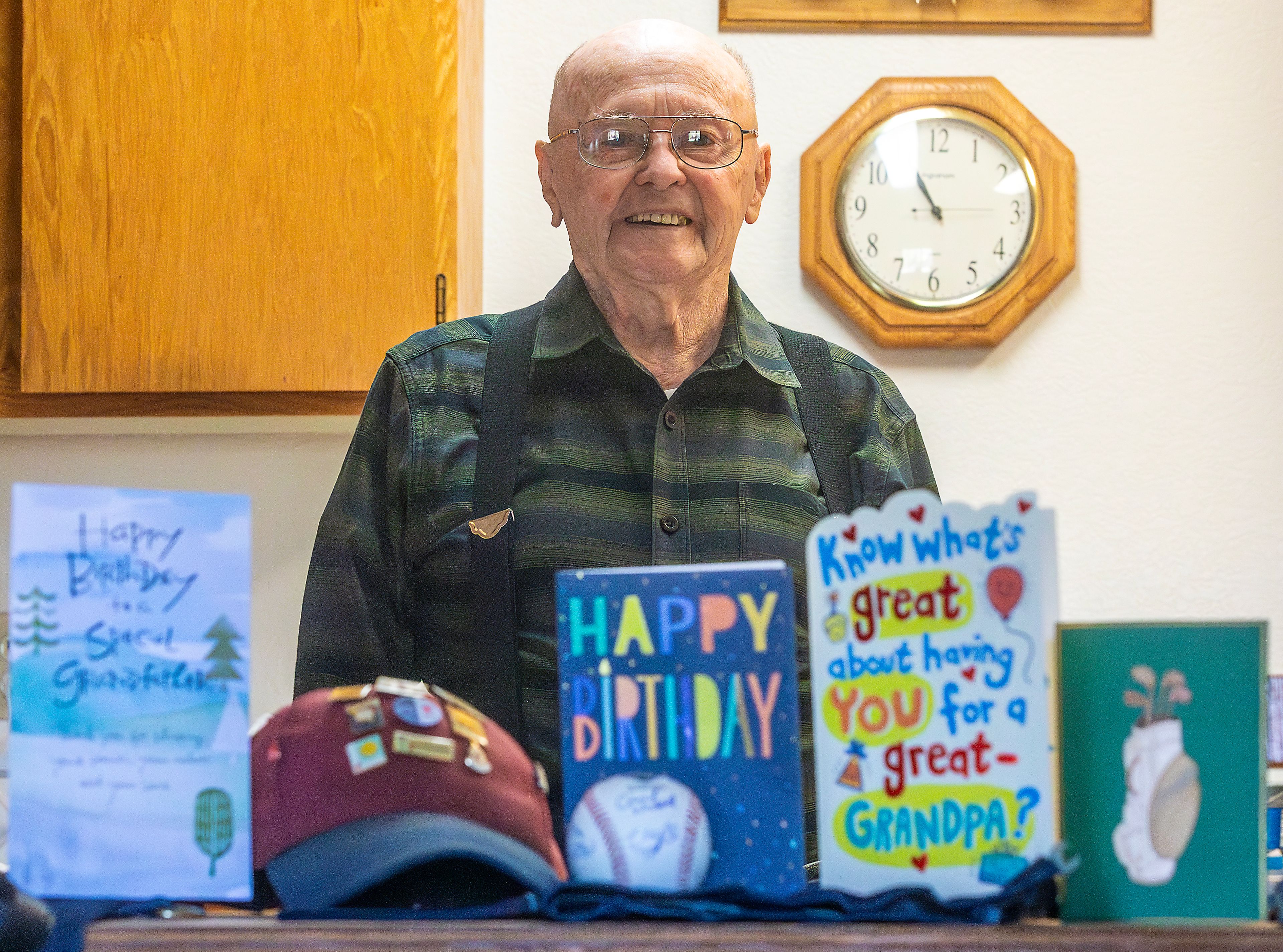 Johnny Wells poses for a photo Tuesday with a collection of memories � several birthday cards he's received for his 100th birthday, along with a hat with pins from times he gave blood and a signed baseball he threw at the NAIA World Series � at his home in Clarkston.