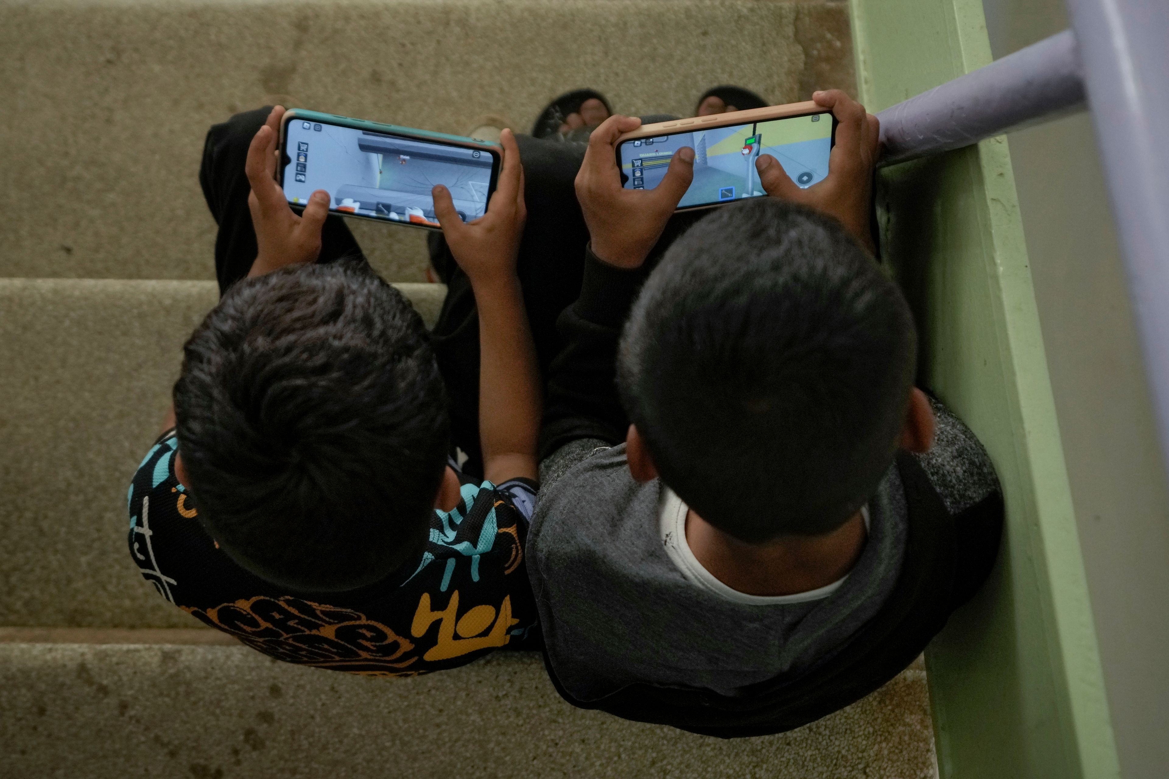 Displaced children play games on their mobile phone at a vocational training center run by the U.N. agency for Palestinian refugees, or UNRWA, in the southern town of Sebline, south of Beirut, Lebanon, Friday, Oct. 4, 2024, after fleeing the Israeli airstrikes in the south. (AP Photo/Bilal Hussein)