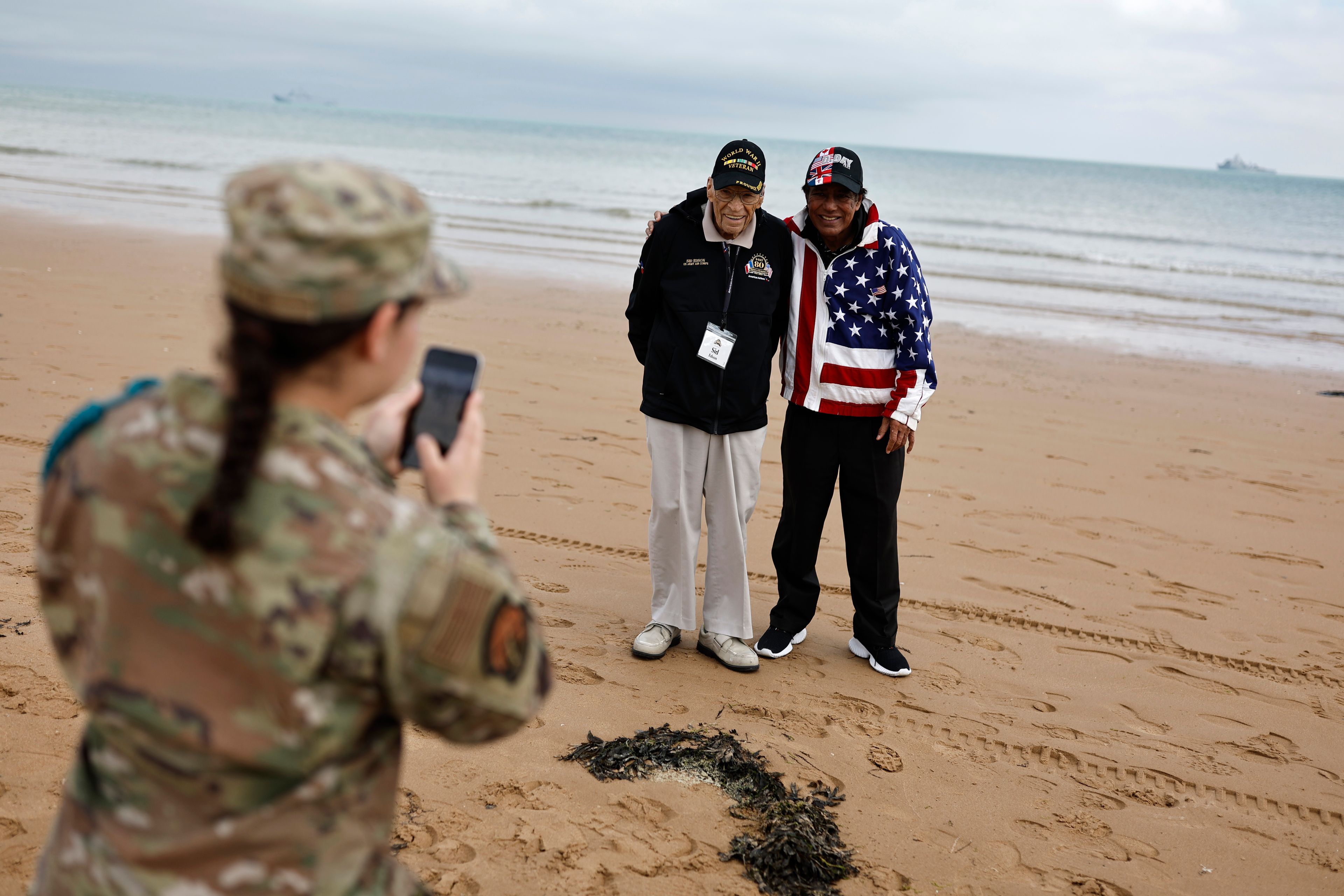 A US soldier takes a photograph of American WWII veteran Sid Edson, center left, during a ceremony on Omaha Beach, Tuesday, June 4, 2024 in Normandy. World War II veterans from across the United States as well as Britain and Canada are in Normandy this week to mark 80 years since the D-Day landings that helped lead to Hitler's defeat. (AP Photo/Jeremias Gonzalez)