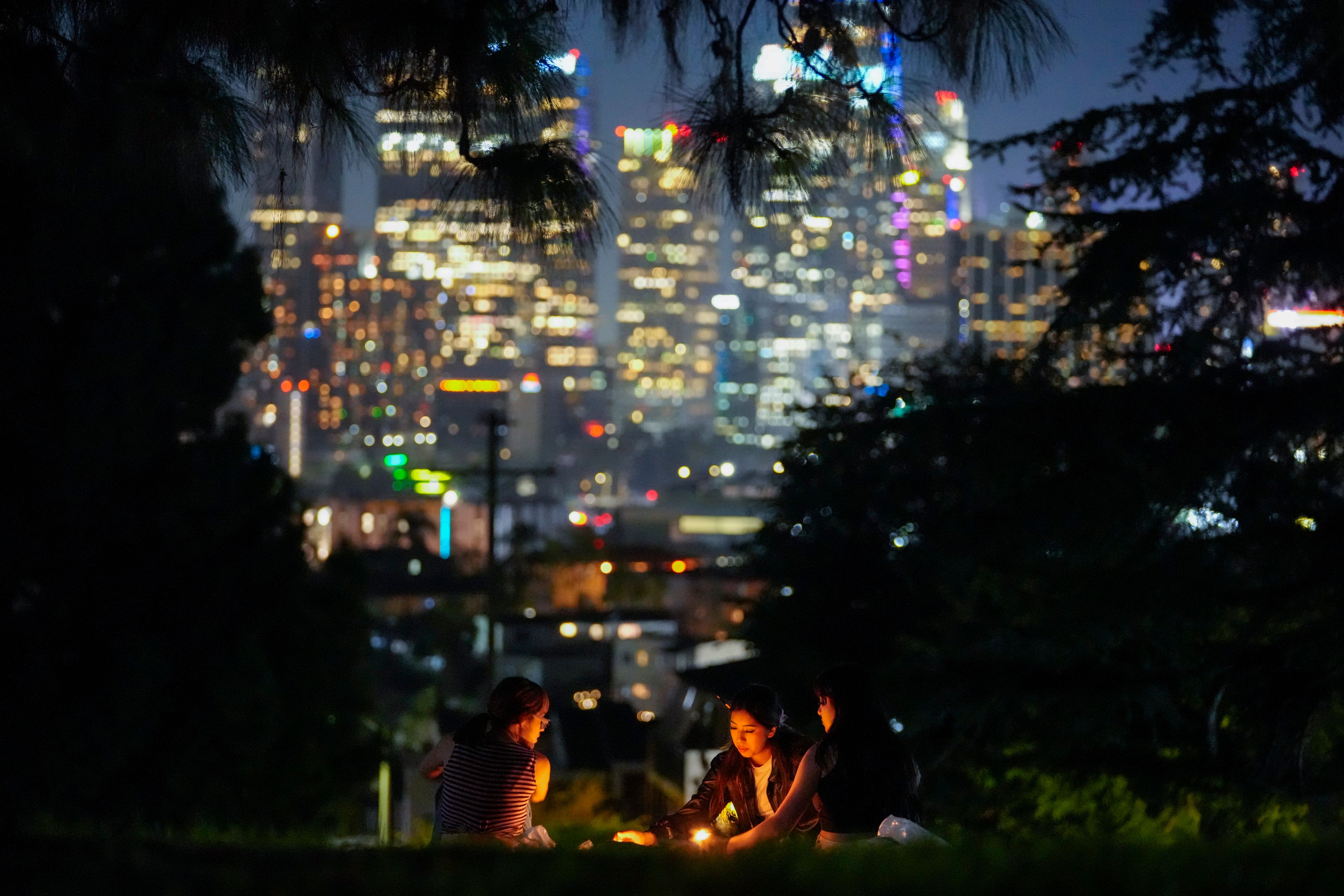 FILE - The downtown Los Angeles skyline gives a backdrop to artists painting under candlelight at Everett Triangle Park, Oct. 22, 2024, in Los Angeles. (AP Photo/Julio Cortez, File)