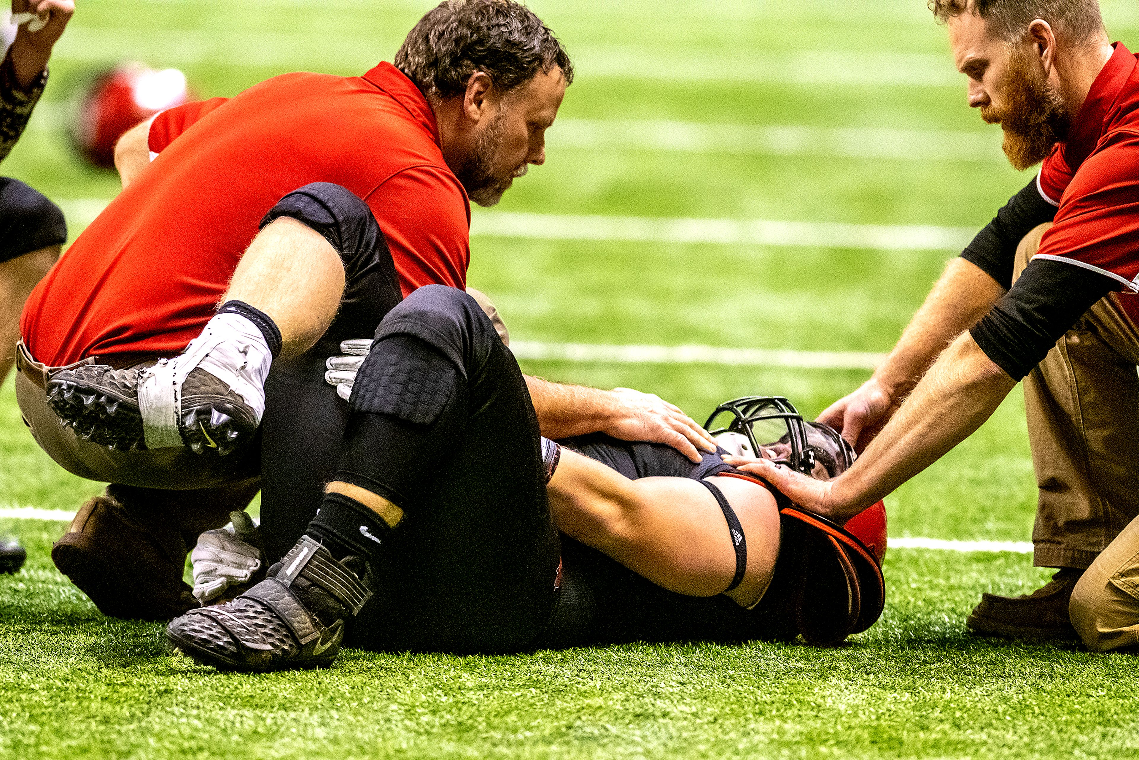 Prairie Head Coach Ryan Hasselstrom (left) attends to Dean Johnson after suffering a broken ankle in the first quarter against Oakley. The Prairie Pirates lost to the Oakley Hornets 42-40 in the Class 1A Division O state semifinal football game at the Kibbie Dome in Moscow on Friday.