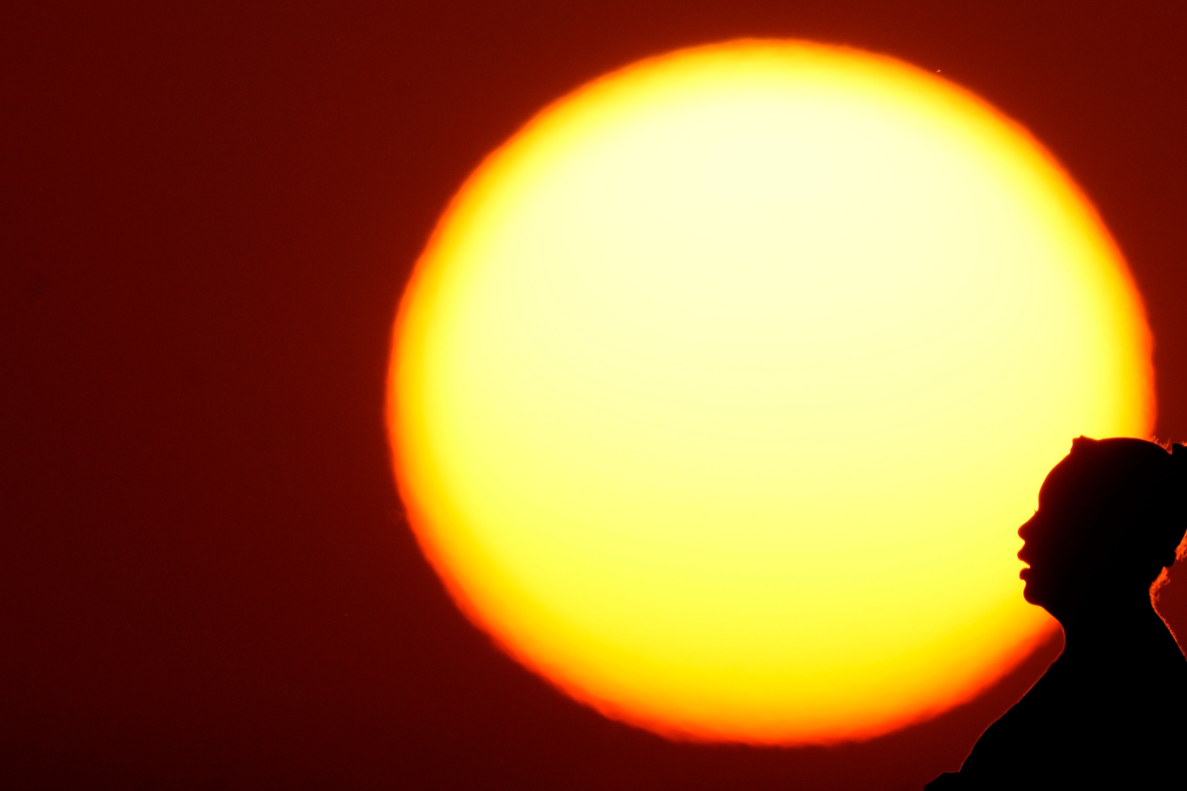 FILE - A woman is silhouetted against the setting sun as triple-digit heat indexes continue in the Midwest, Aug. 20, 2023, in Kansas City, Mo. The rate Earth is warming hit an all-time high in 2023 with 92% of last year’s surprising record-shattering heat caused by humans, top scientists calculated.