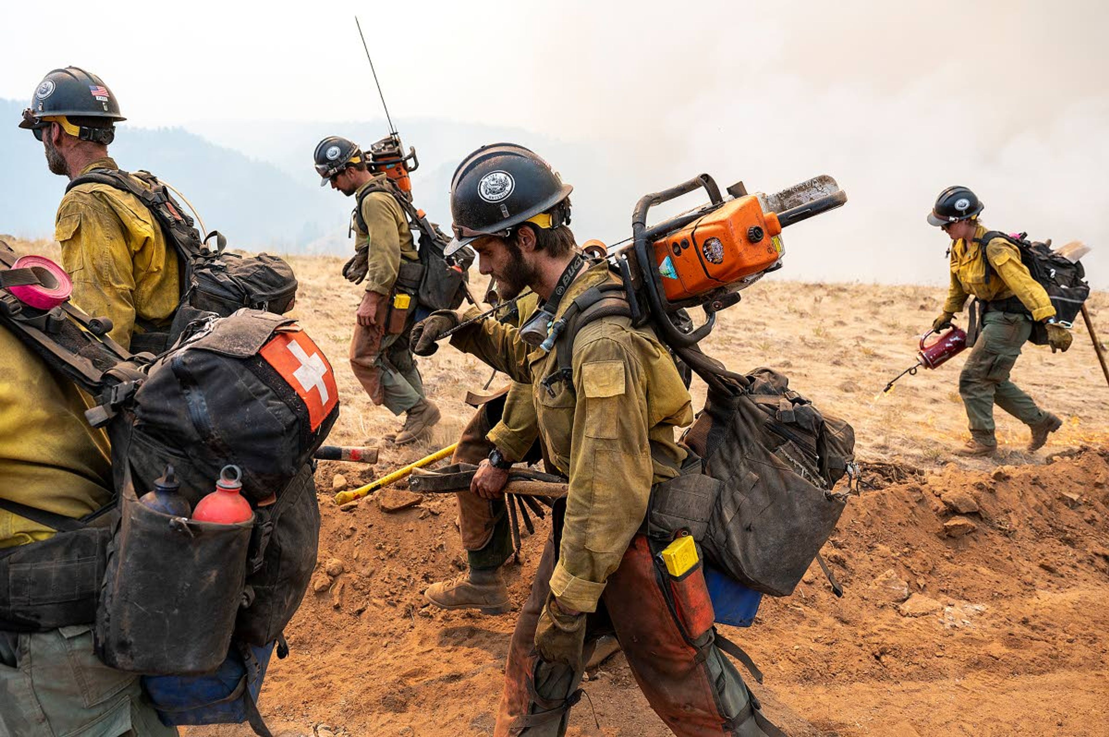 A crew of wildland firefighters walks along a road created with a bulldozer as a fire-line buffer as they set fire to the brush on Monday afternoon at the Lick Creek Fire southwest of Asotin. The crew was lighting the brush on fire in order to burn off the fuel for the main fire which was headed south through the South Fork drainage below them.