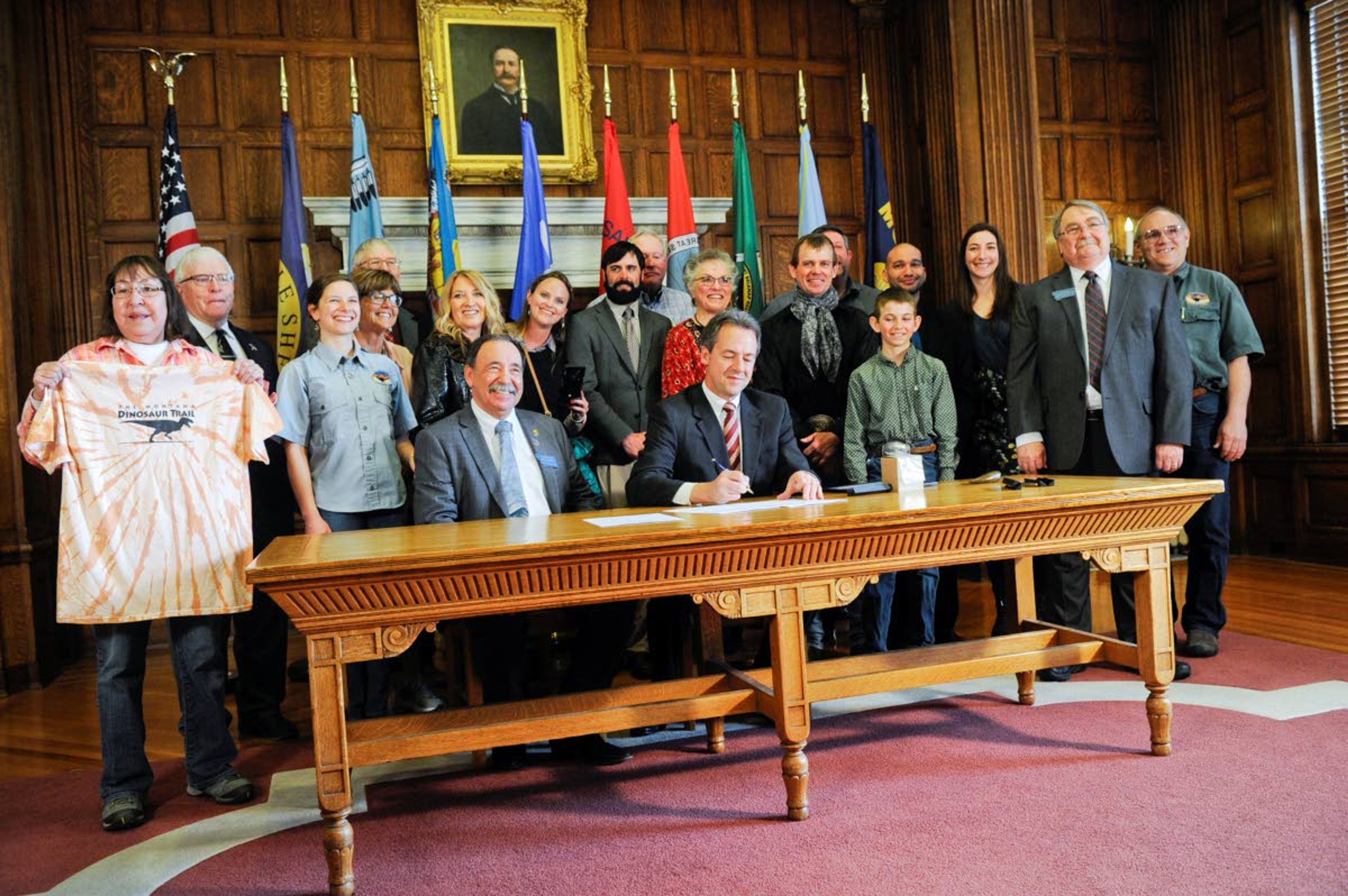 Montana Gov. Steve Bullock, center, signs a bill to clarify that fossils are part of a property's surface rights, not its mineral rights, unless a contract separating the ownership says otherwise, Tuesday, April 16, 2019, at the State Capitol in Helena, Mont. (Thom Bridge/Independent Record via AP)