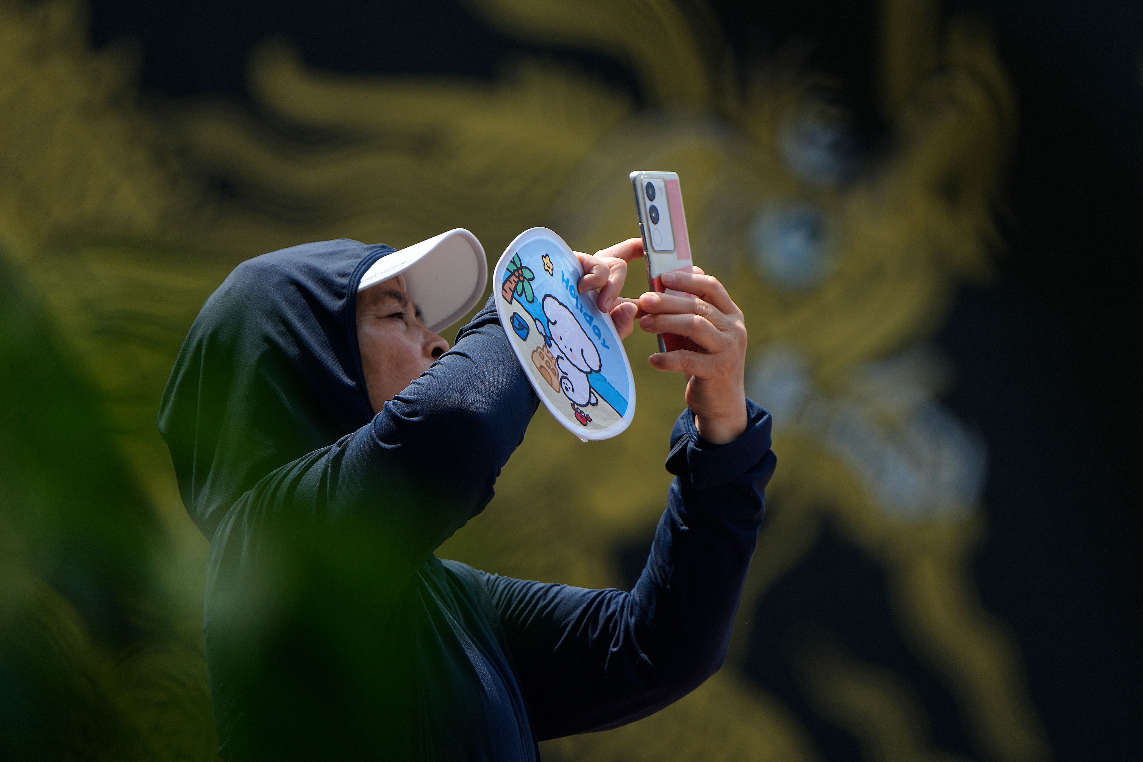 A woman uses a smartphone to film the Dragon Boat festival at a canal in Tongzhou, on the outskirts of Beijing, Monday, June 10, 2024. The Duanwu festival, also known as the Dragon Boat festival, falls on the fifth day of the fifth month of the Chinese lunar calendar and is marked by celebrations like eating rice dumplings and racing dragon boats.