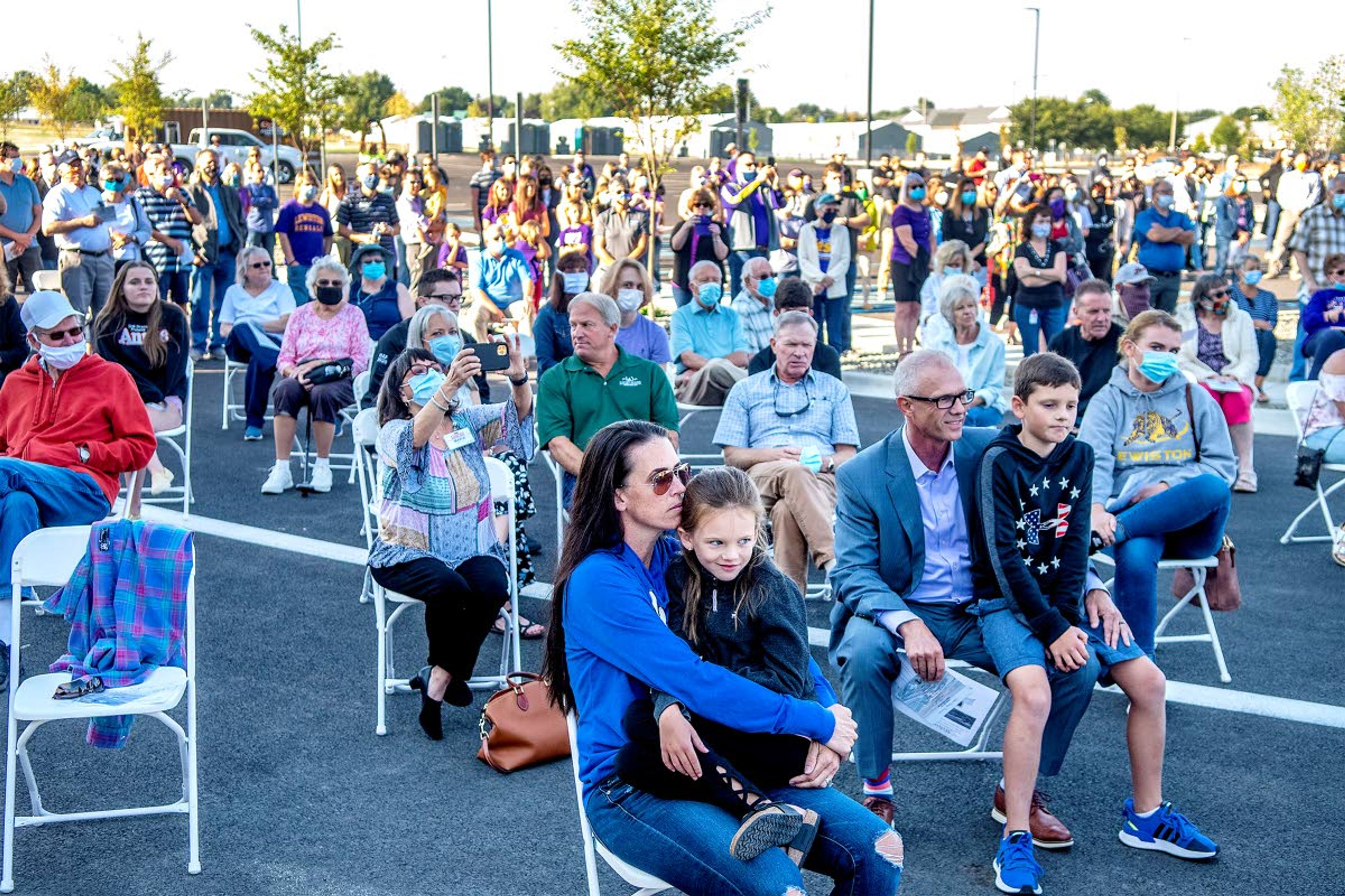 Laney Roy, 7, sits on the lap of her mother, Sara Roy, as they listen to speakers at the ribbon-cutting event for the new Lewiston High School on Friday morning.