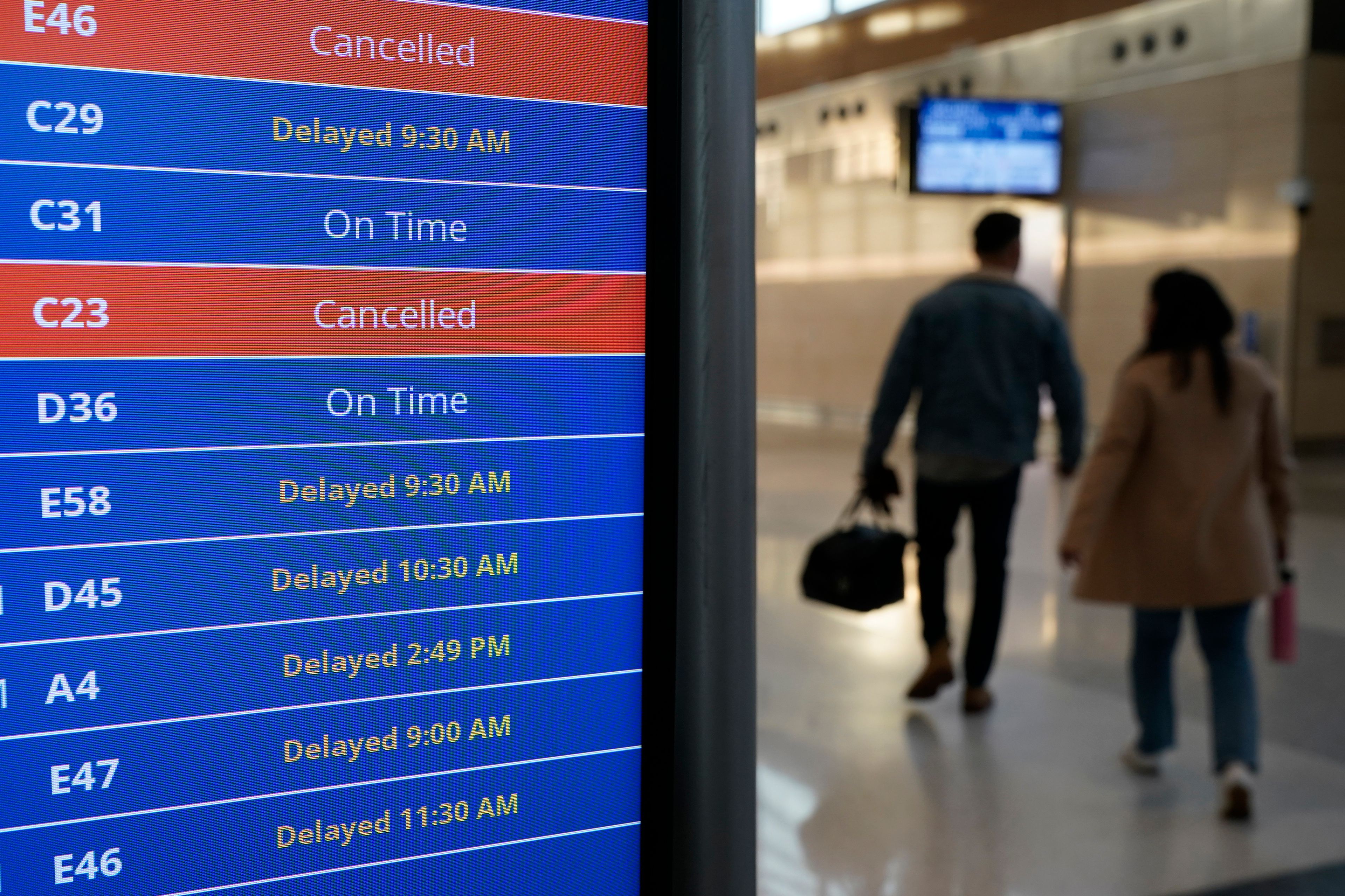 Travelers walk as a video board shows flight delays and cancellations at Ronald Reagan Washington National Airport in Arlington, Va., Wednesday.